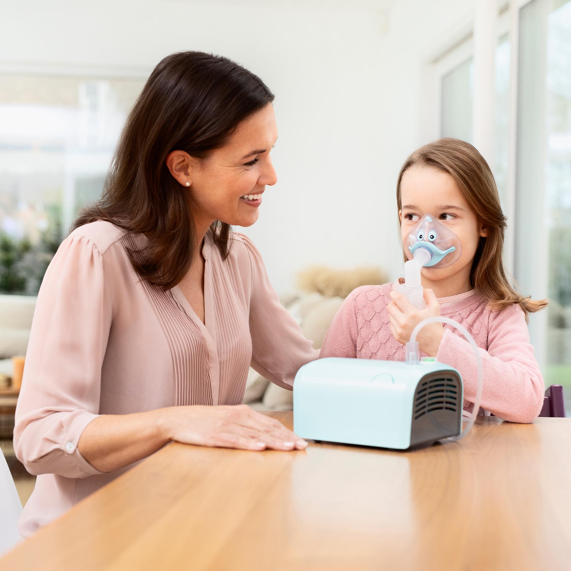 A woman and a child with an inhaler, sitting at a table in a bright room.