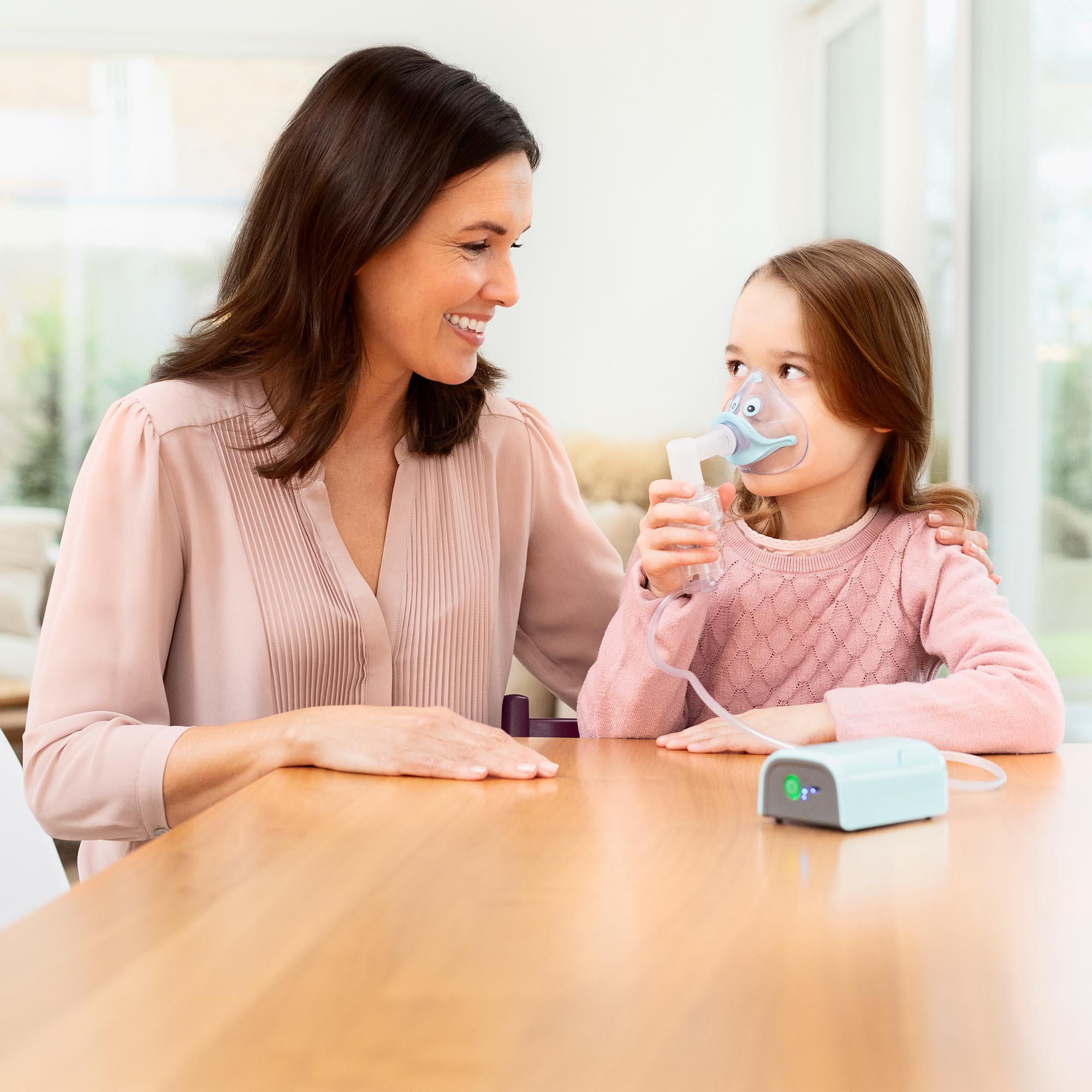 Kobieta i mała dziewczynka używają nebulizatora. Dziewczynka patrzy na swoją matkę.