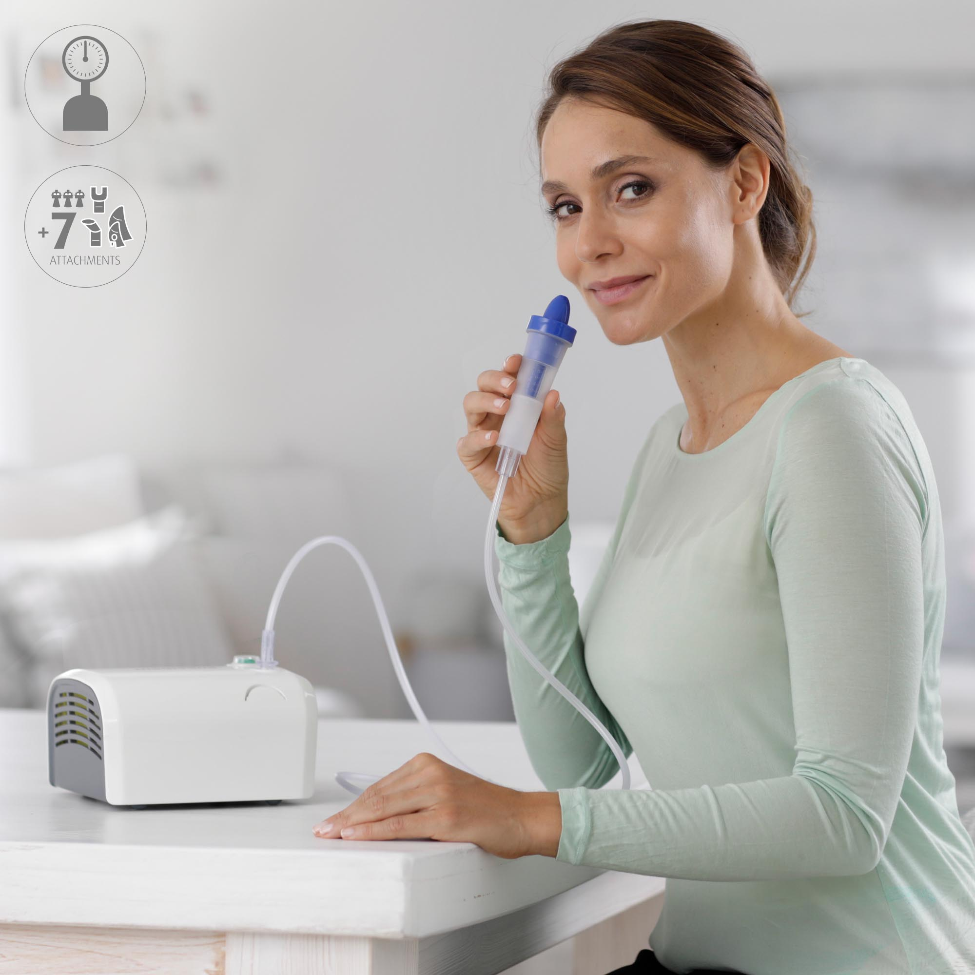 Kobieta trzyma maskę inhalatora. Na stole stoi biała maszyna do nebulizacji. Uśmiechnięta.