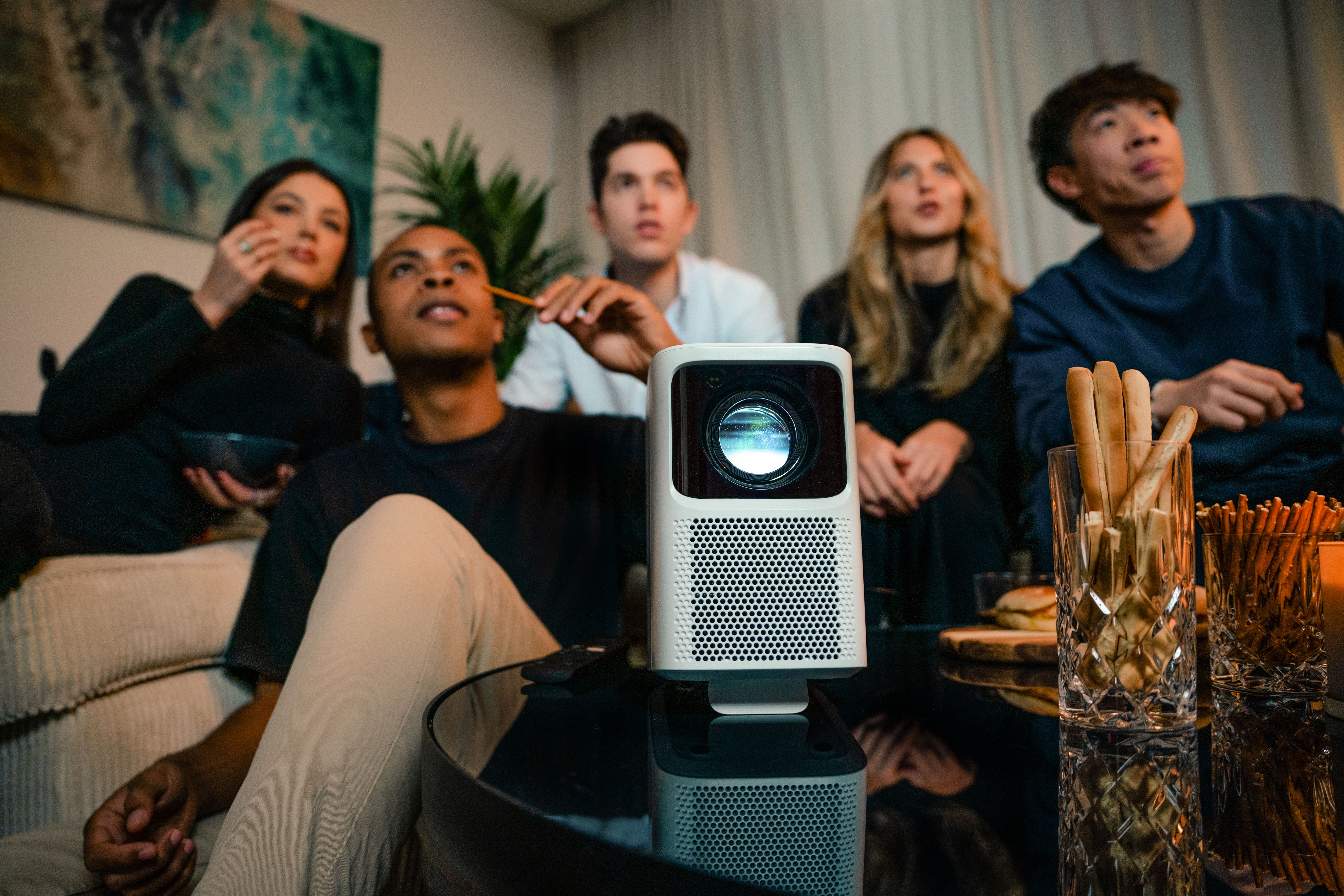 Group of people watching a projector screen, holding snacks.