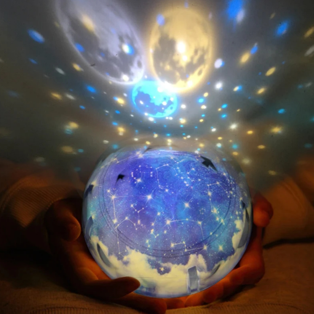 Hände halten einen leuchtenden Globus mit Sternenhimmel-Projektion, mondähnlichen Lichtern.