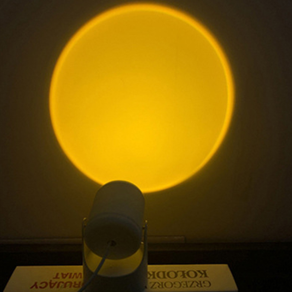 Ein gelbes kreisförmiges Licht, das die Sonne nachahmt, scheint auf eine dunkle Wand. Darunter ein Projektor.