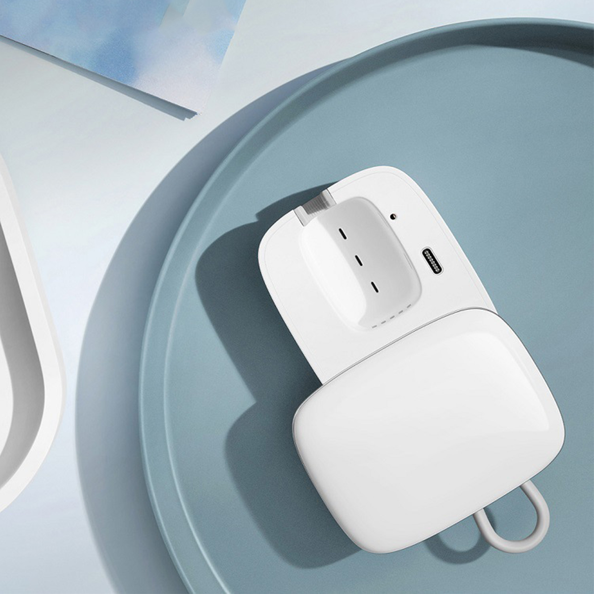 Ein weißes, offenes, abgerundetes rechteckiges Gerät mit einem USB-C-Anschluss, das auf einem blauen, ovalen Tablett liegt.