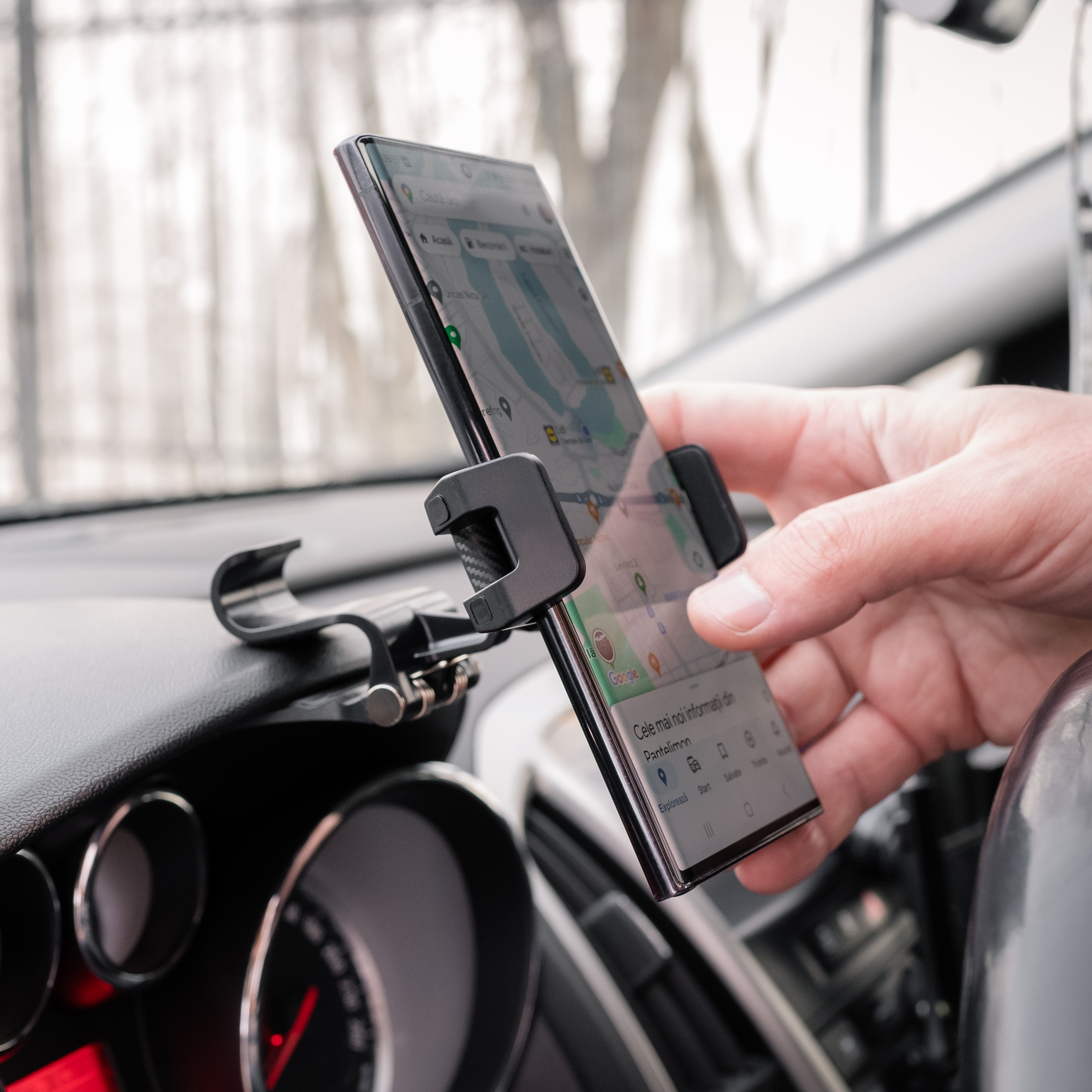 Telefon w uchwycie samochodowym, aplikacja map na ekranie, dłoń regulująca.