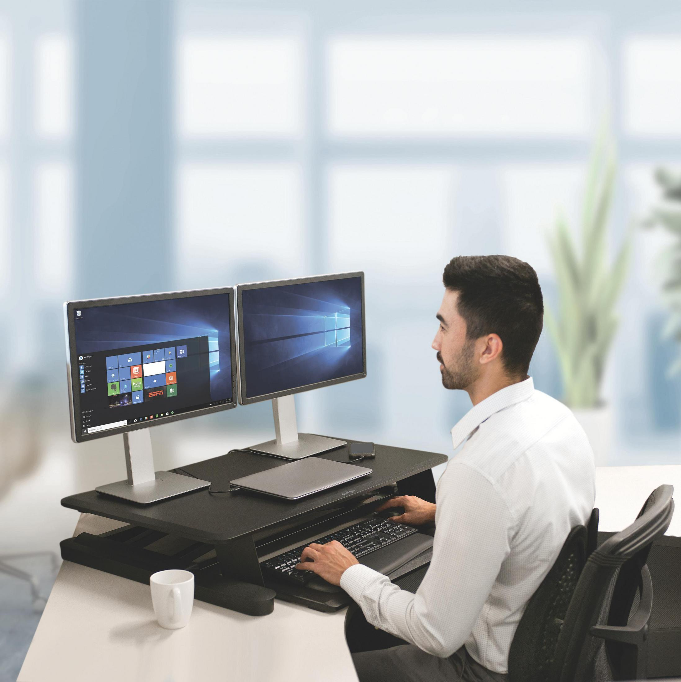 Ein Mann an einem Stehpult mit zwei Monitoren, der auf einer Tastatur tippt.