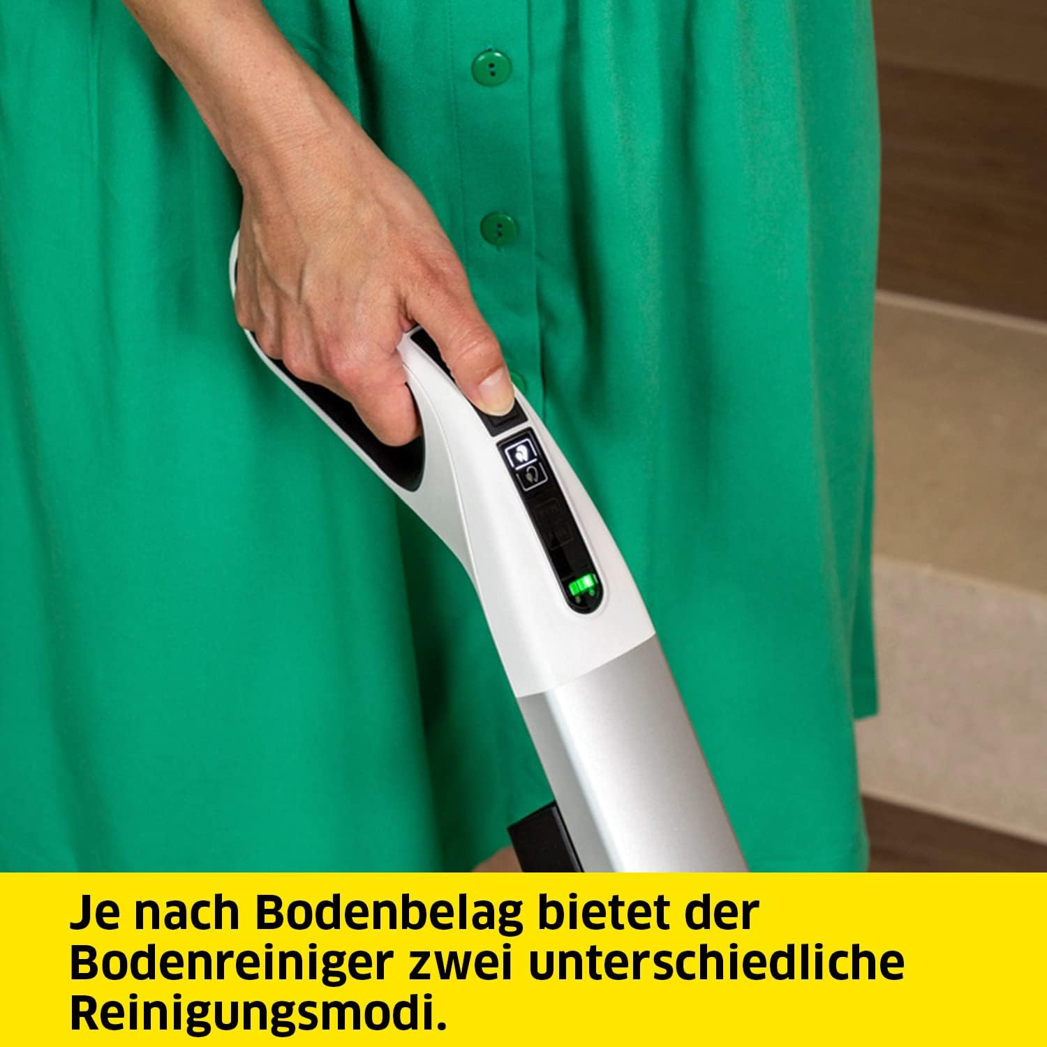 Ręka naciskająca przycisk na białej i srebrnej myjce do podłóg, w pobliżu zielonej sukienki.