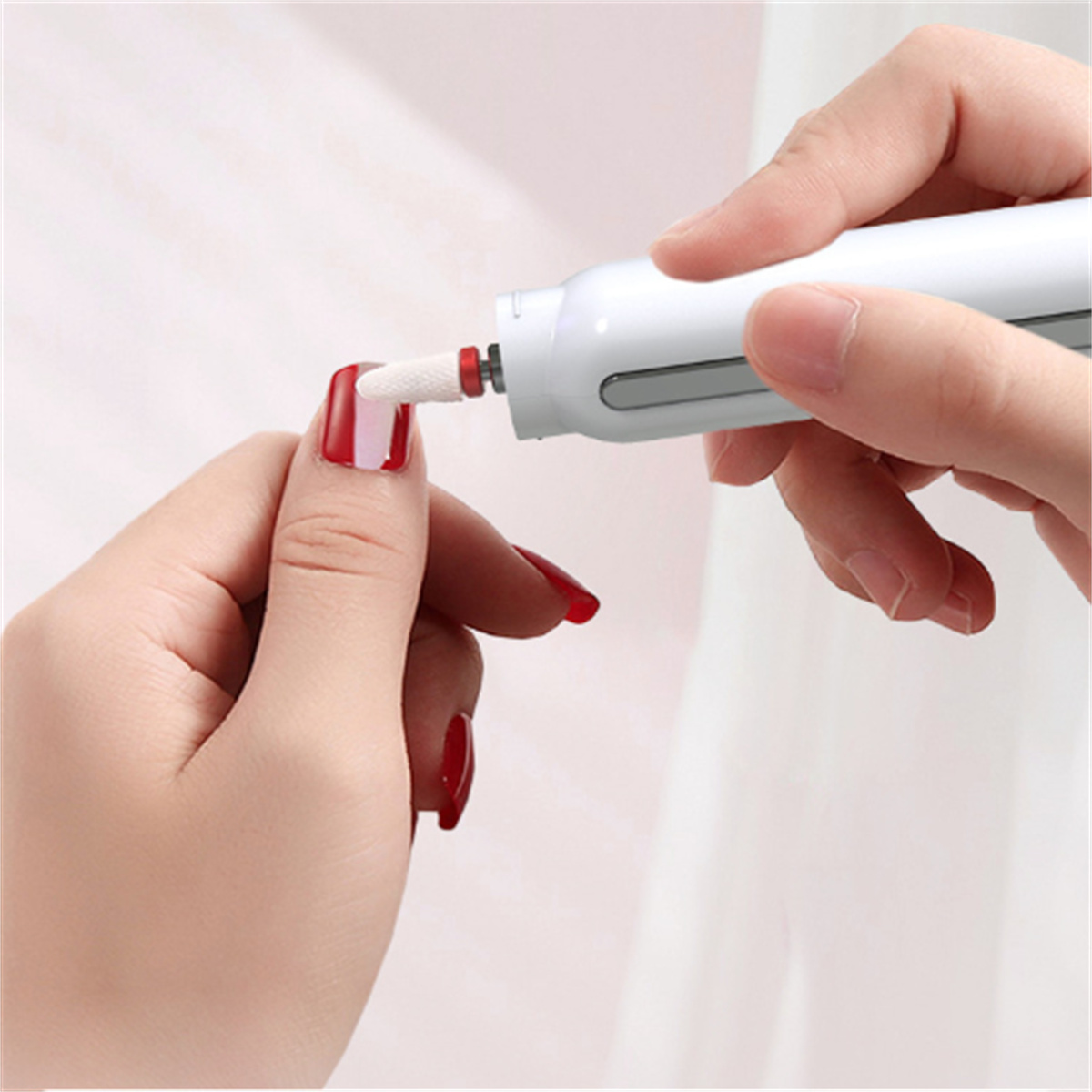 Hände einer Person, die einen weißen Nagelbohrer verwenden, um einen rot lackierten Nagel zu formen.
