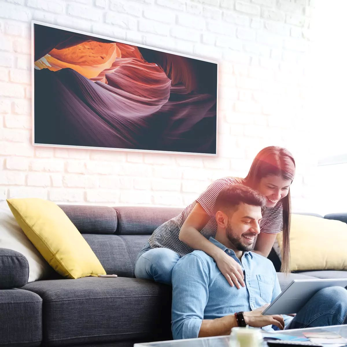 Paar auf einem grauen Sofa, das einen Tablet-PC betrachtet. Ein großes gerahmtes Bild hängt an der Wand.