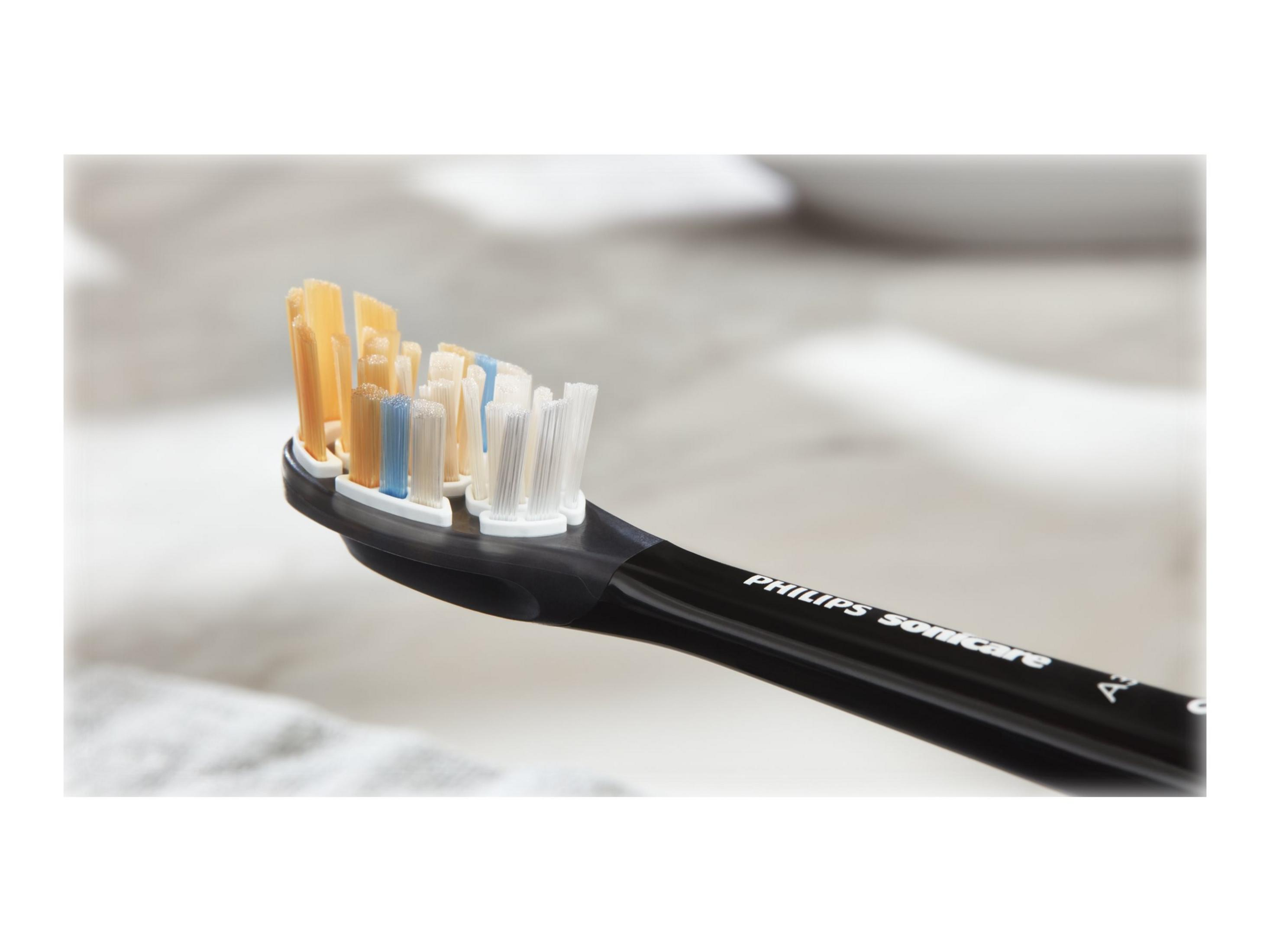 Zbliżenie główki szczoteczki do zębów z żółtym, niebieskim i białym włosiem, czarny uchwyt.