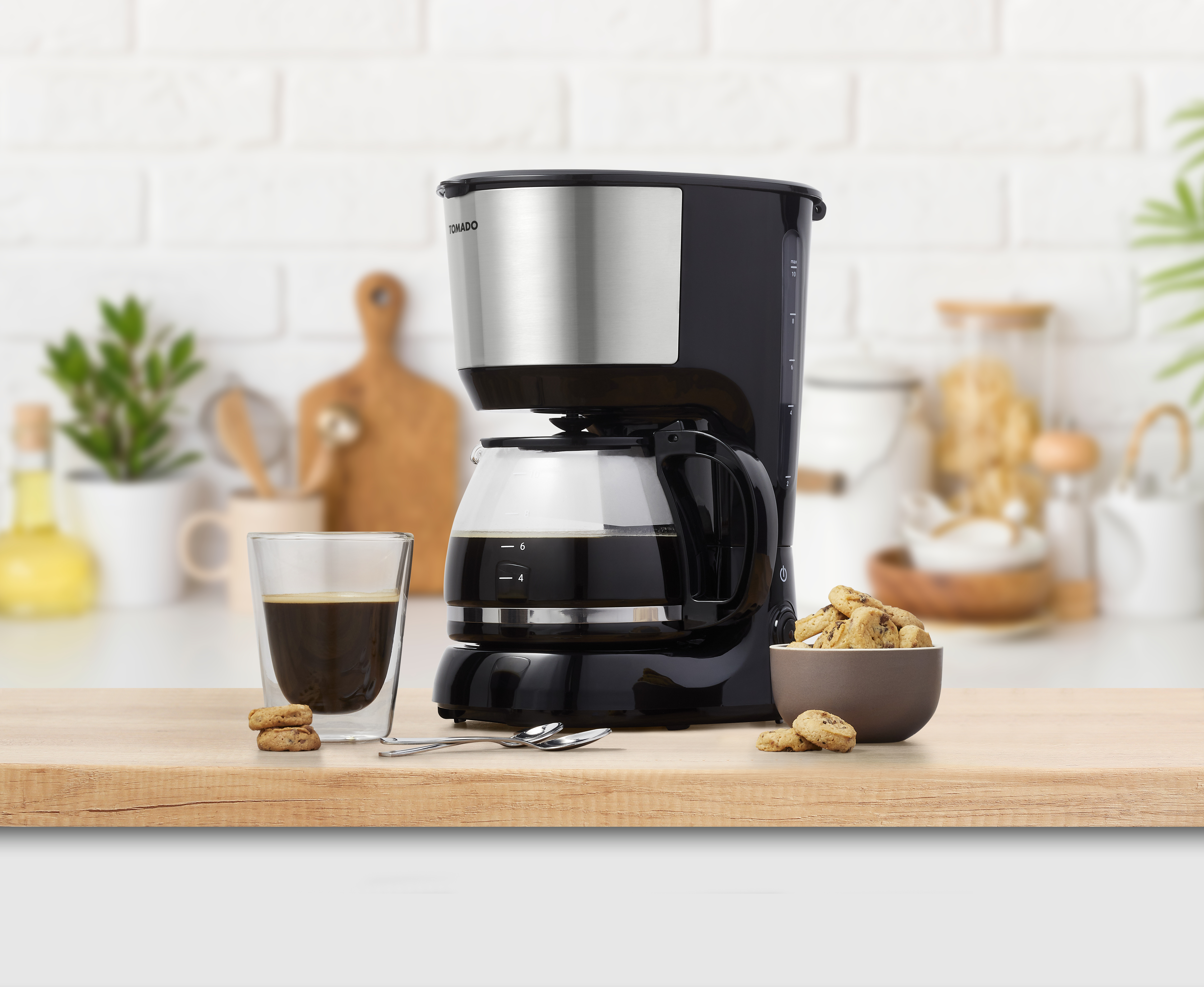 Black and silver coffee maker with a glass carafe. There is a glass of coffee and cookies.