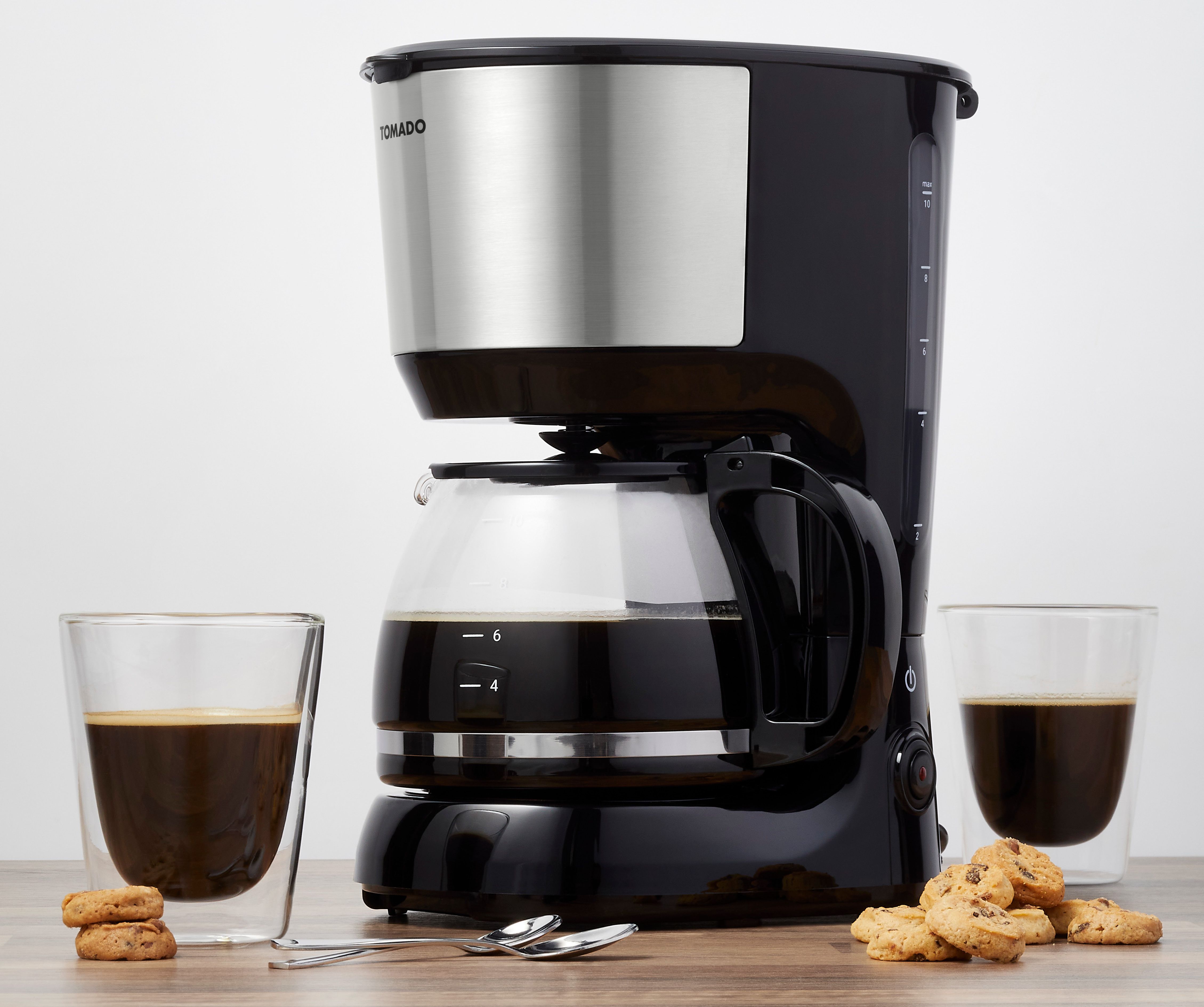 Black coffee maker with glass carafe, coffee, cookies, and two clear glasses. White background.