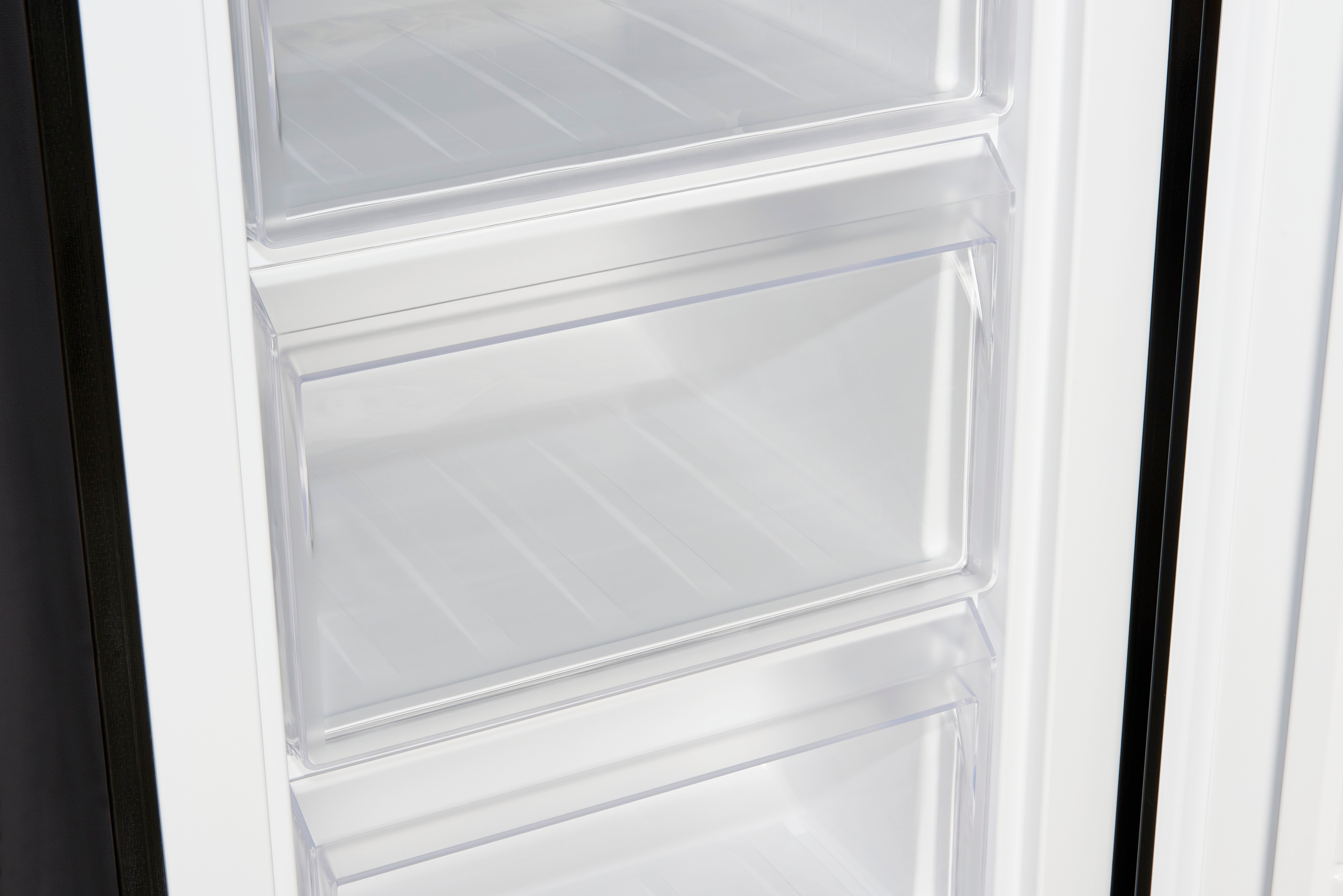 Ein geöffneter Kühlschrank mit drei transparenten Schubladen im Inneren, beleuchtet durch Innenlicht.