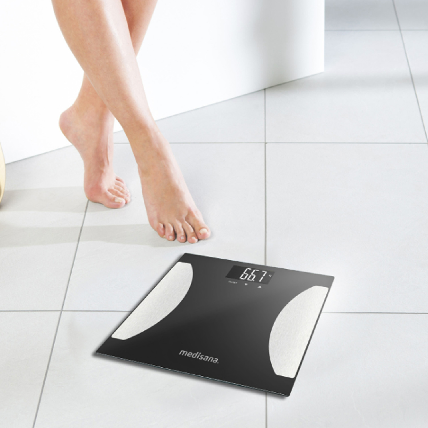 Bilancia digitale nera con display del peso. Piedi scalzi su pavimento piastrellato. Sfondo bianco.