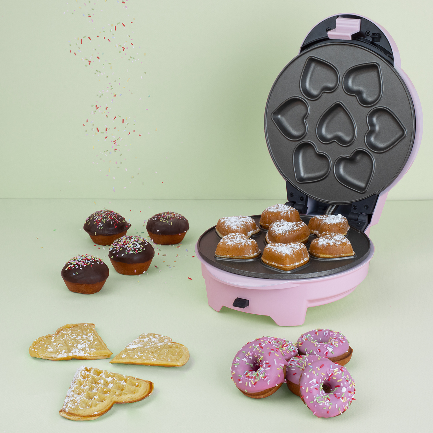 Máquina para hacer gofres rosa con gofres en forma de corazón. Se ven chispas y productos horneados.