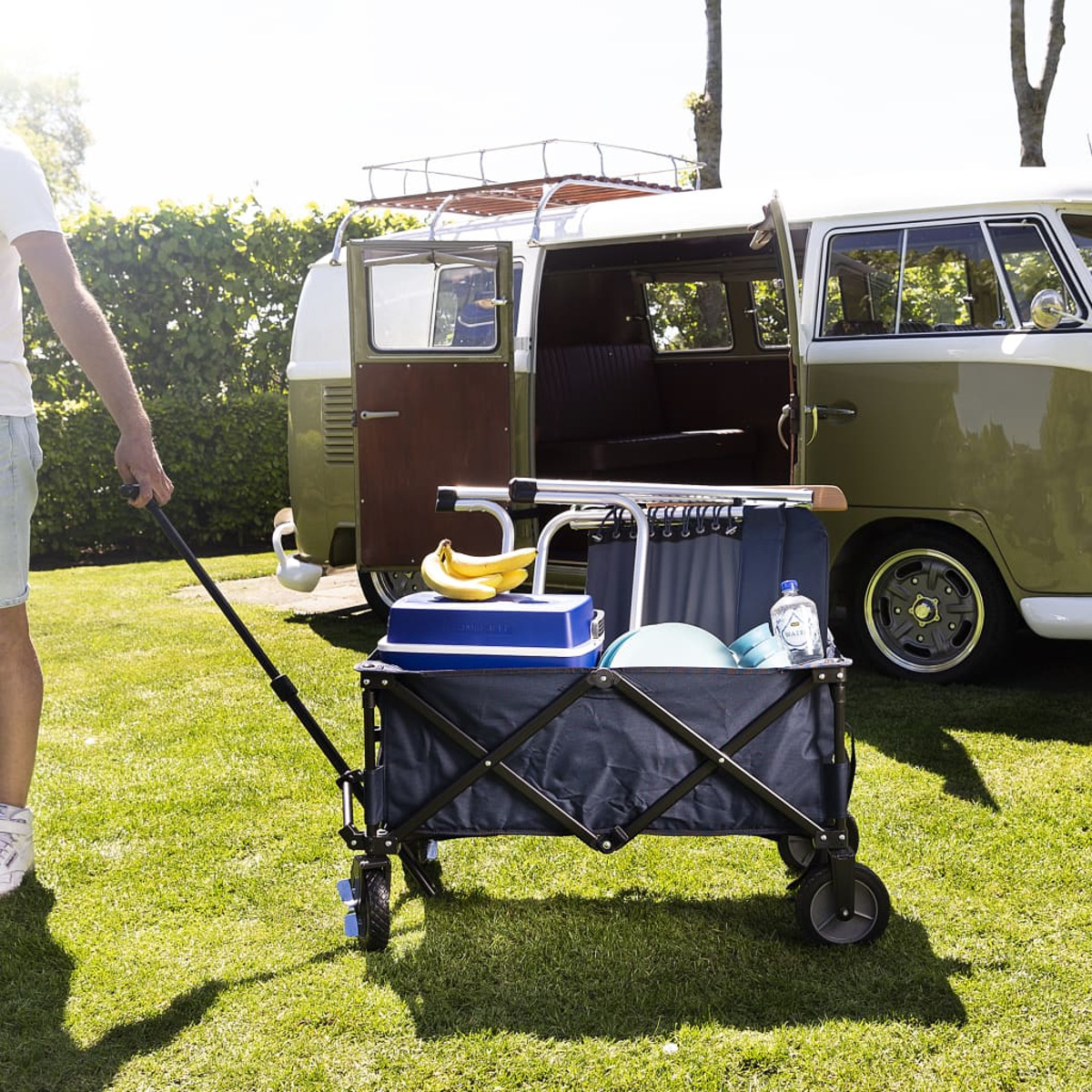 Ein Mann zieht einen Wagen mit Picknickzubehör neben einem Oldtimer-Bus.