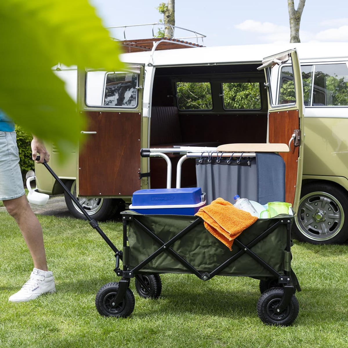 Carrello verde con attrezzatura da campeggio vicino a un vecchio furgone VW.