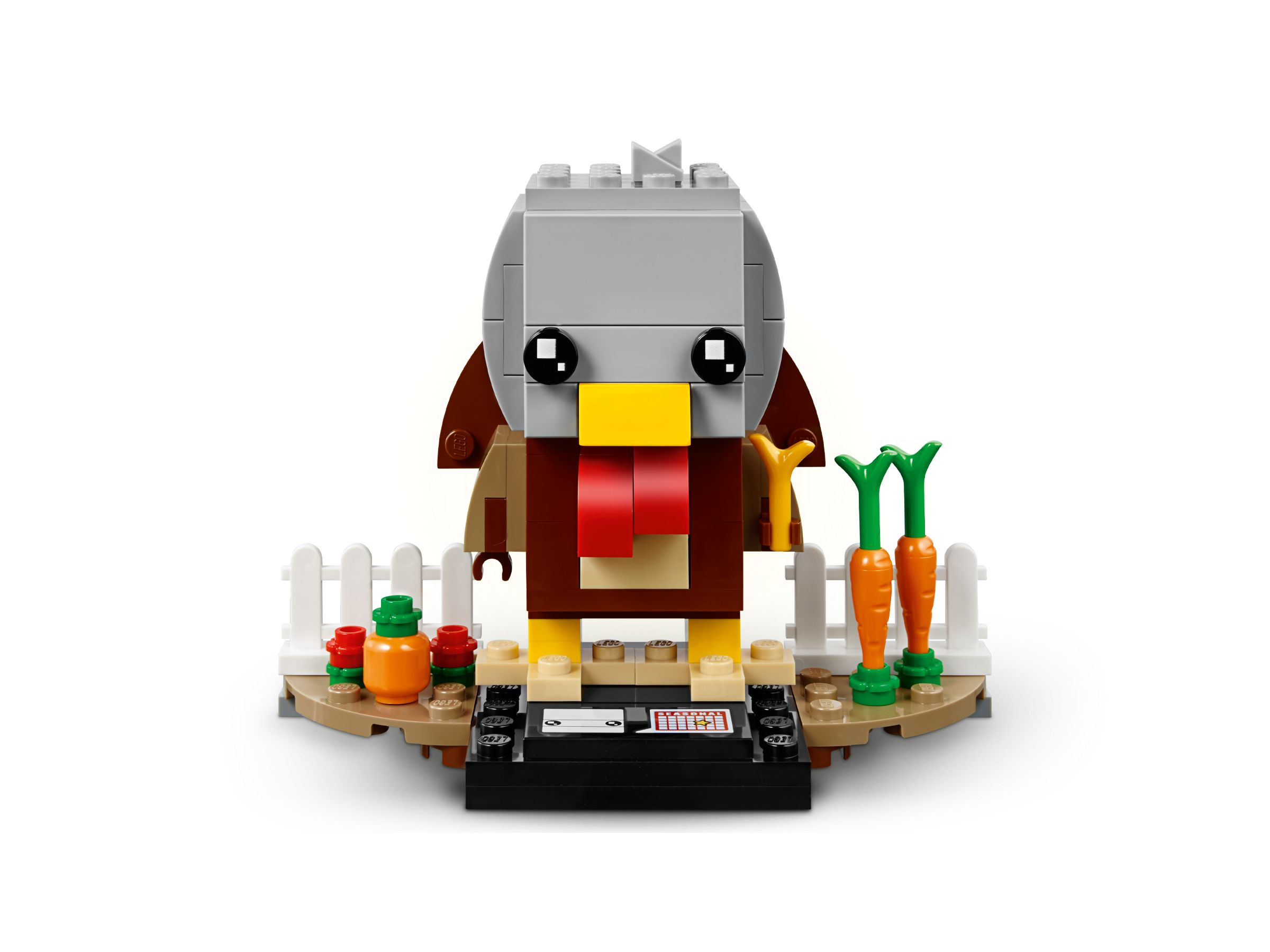 Lego-Truthahnfigur mit weißem Lattenzaun, Karotten und Grundplatte.