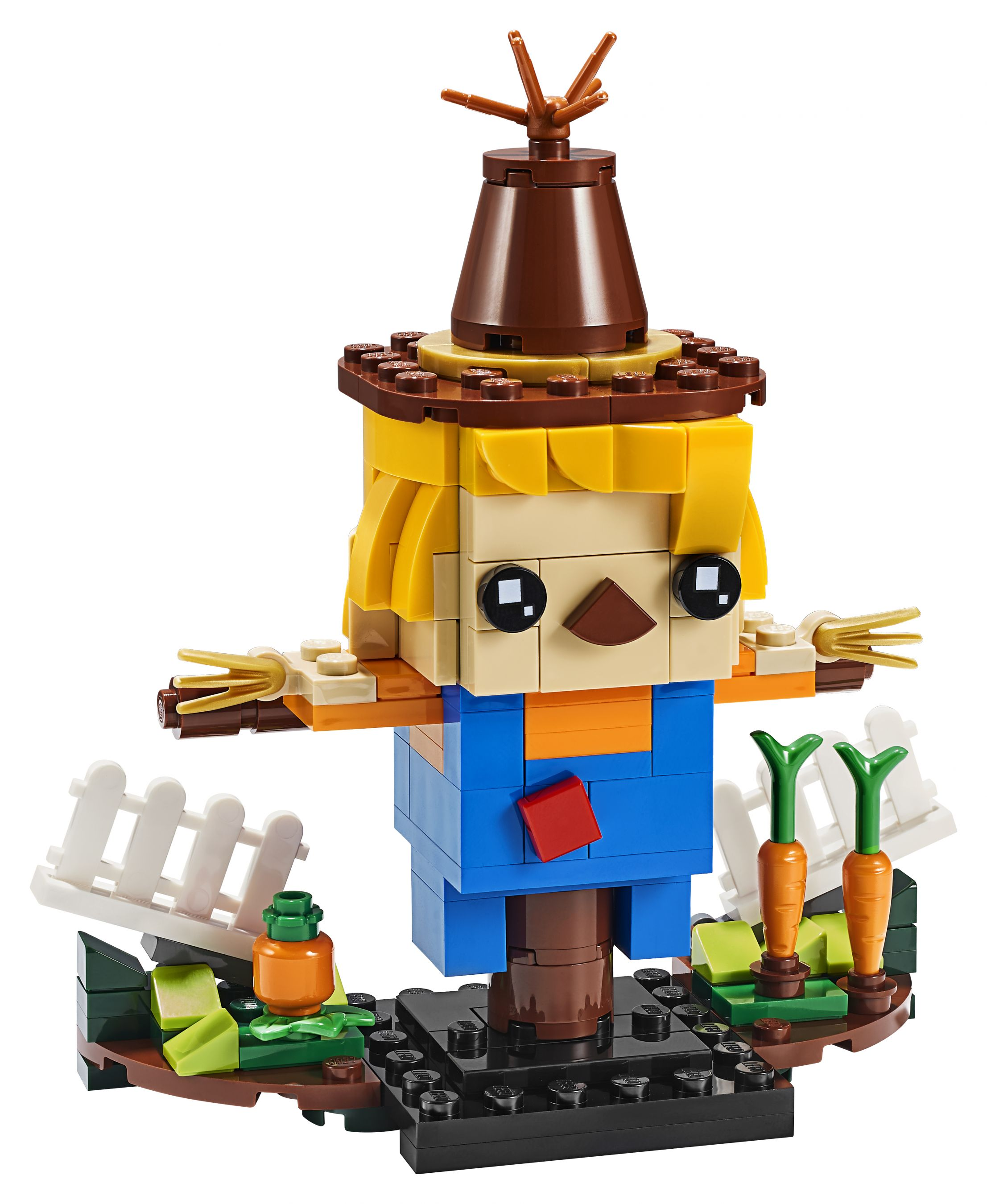 Eine Lego-Figur einer Vogelscheuche, aus Blöcken, die in einer Gartenszene mit Karotten und einem Zaun steht.