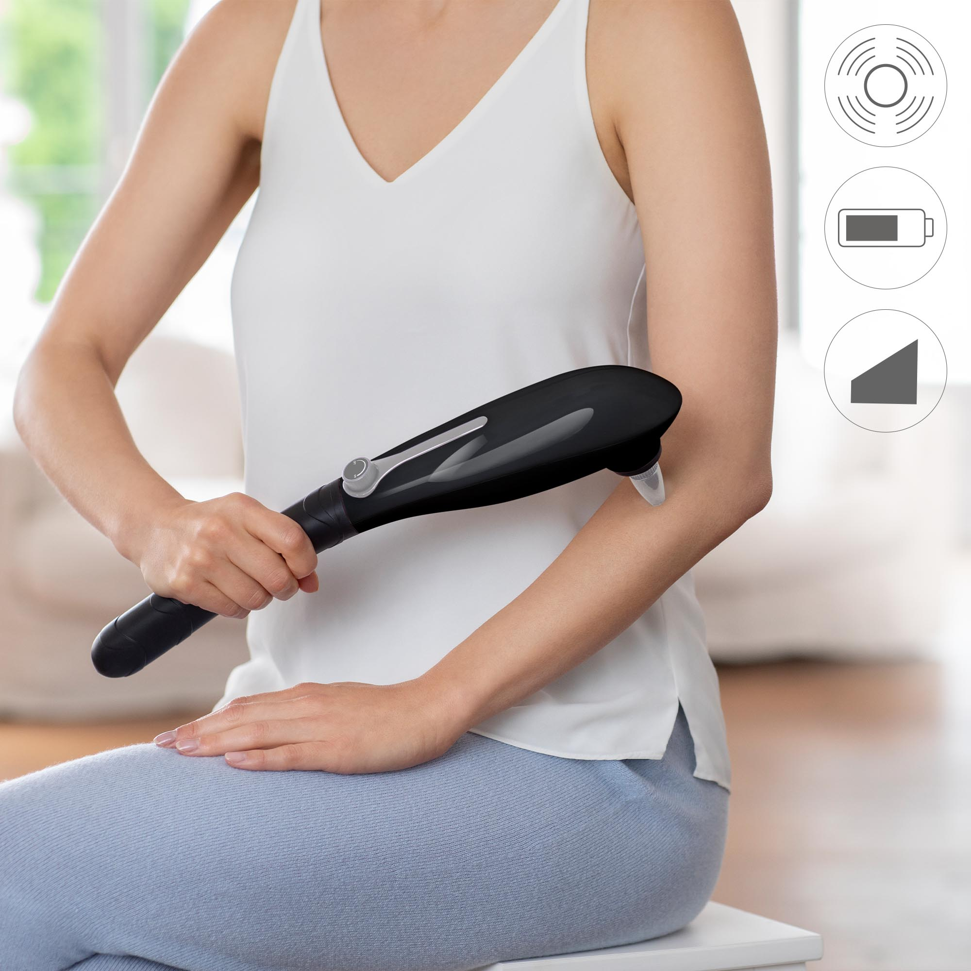 Una mujer usando un dispositivo de masaje negro en su brazo. Los iconos indican vibración, batería y volumen.
