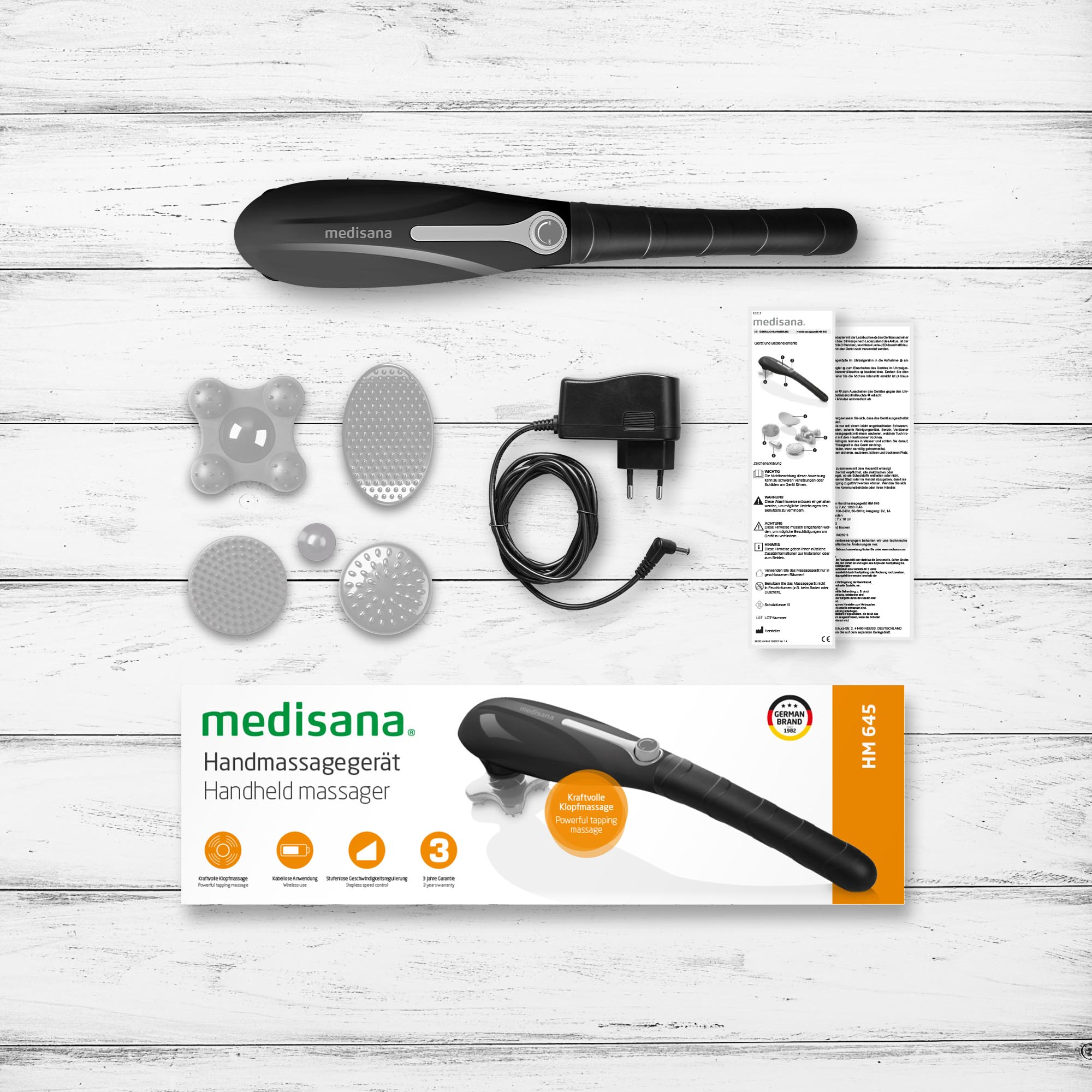 Un masajeador de mano con accesorios y embalaje. Hay una descripción general del producto en la caja.