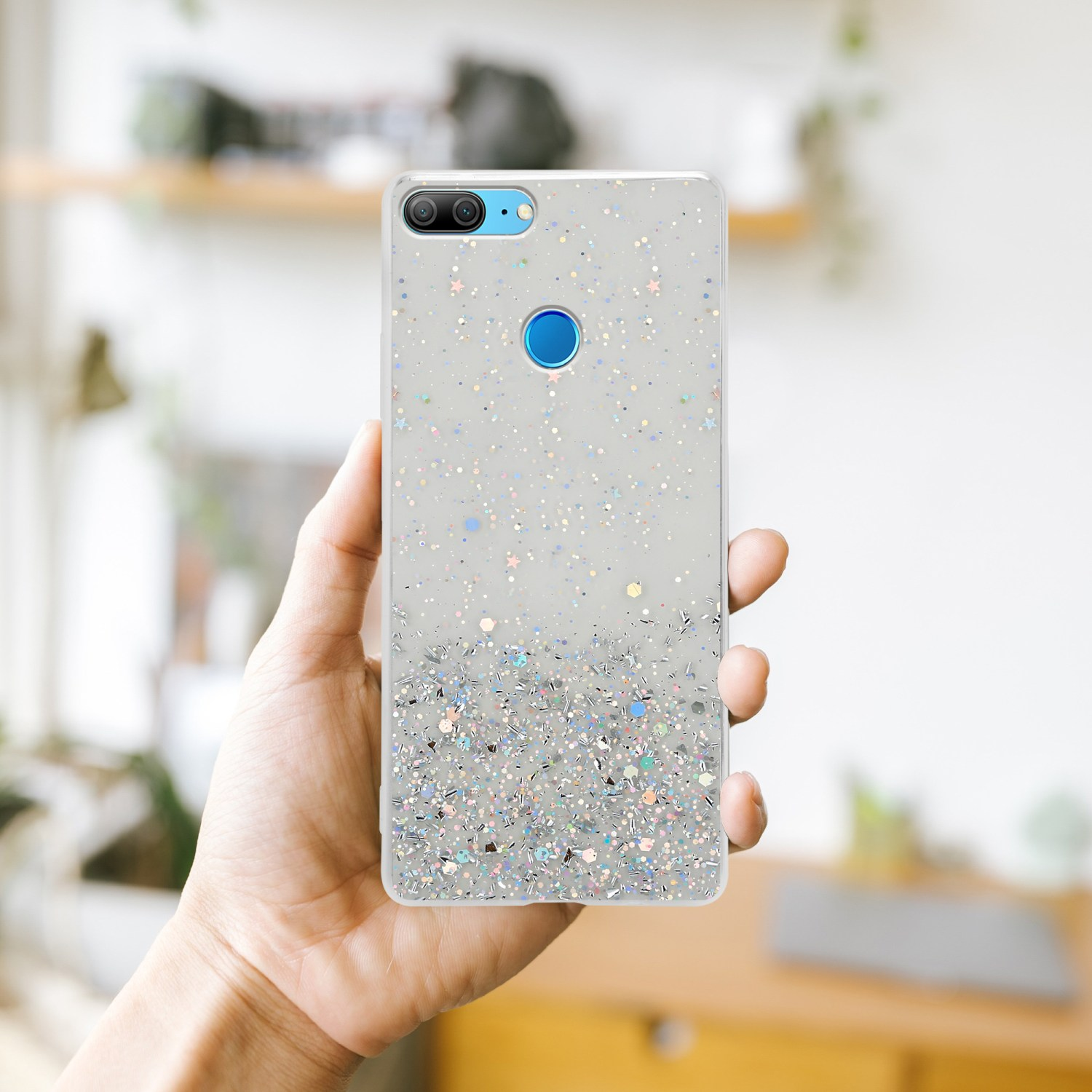 Una mano che tiene una custodia per telefono con un design glitterato, con uno sfondo sfocato.