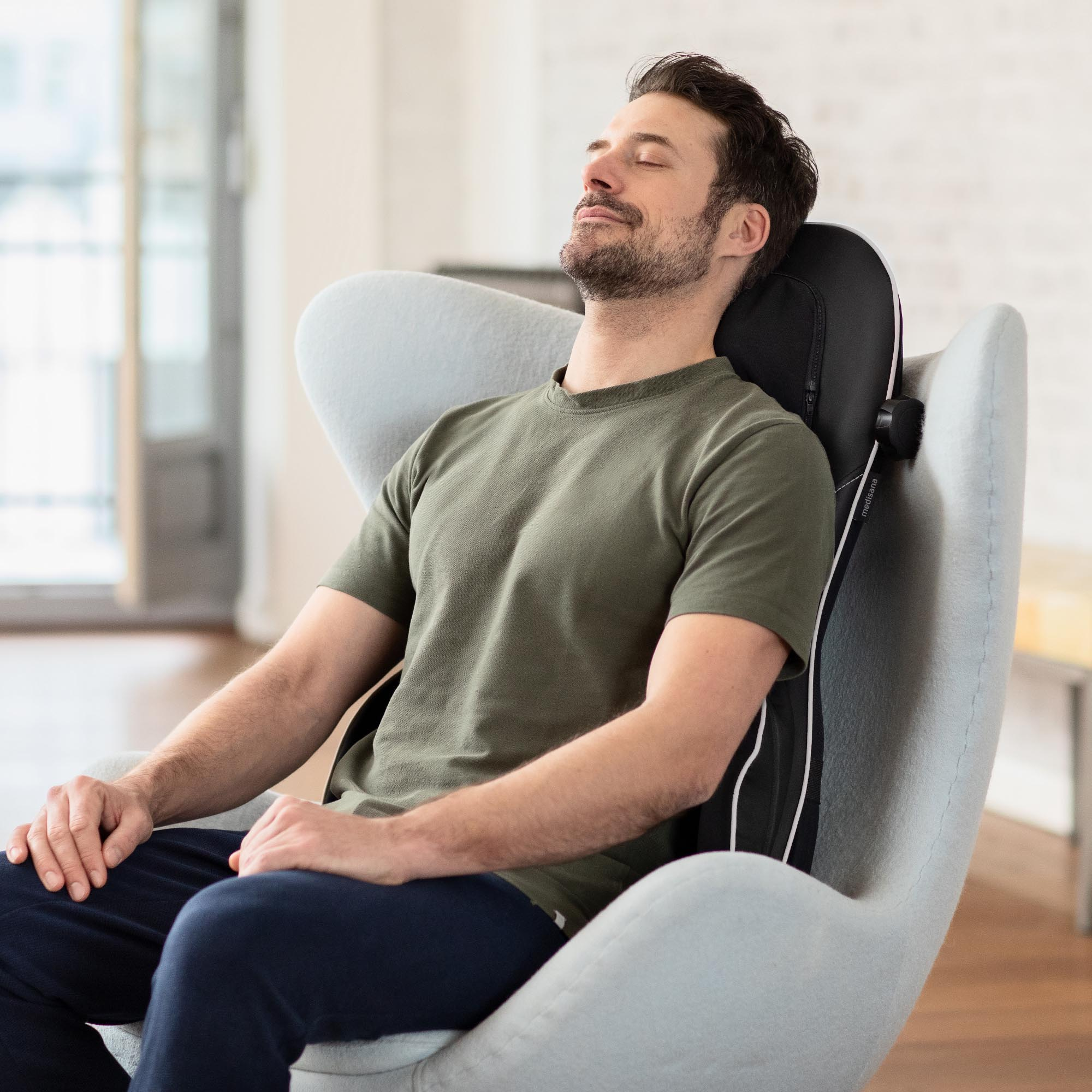 Mężczyzna w zielonej koszuli siedzi na szarym krześle z masażerem pleców. Ma zamknięte oczy.