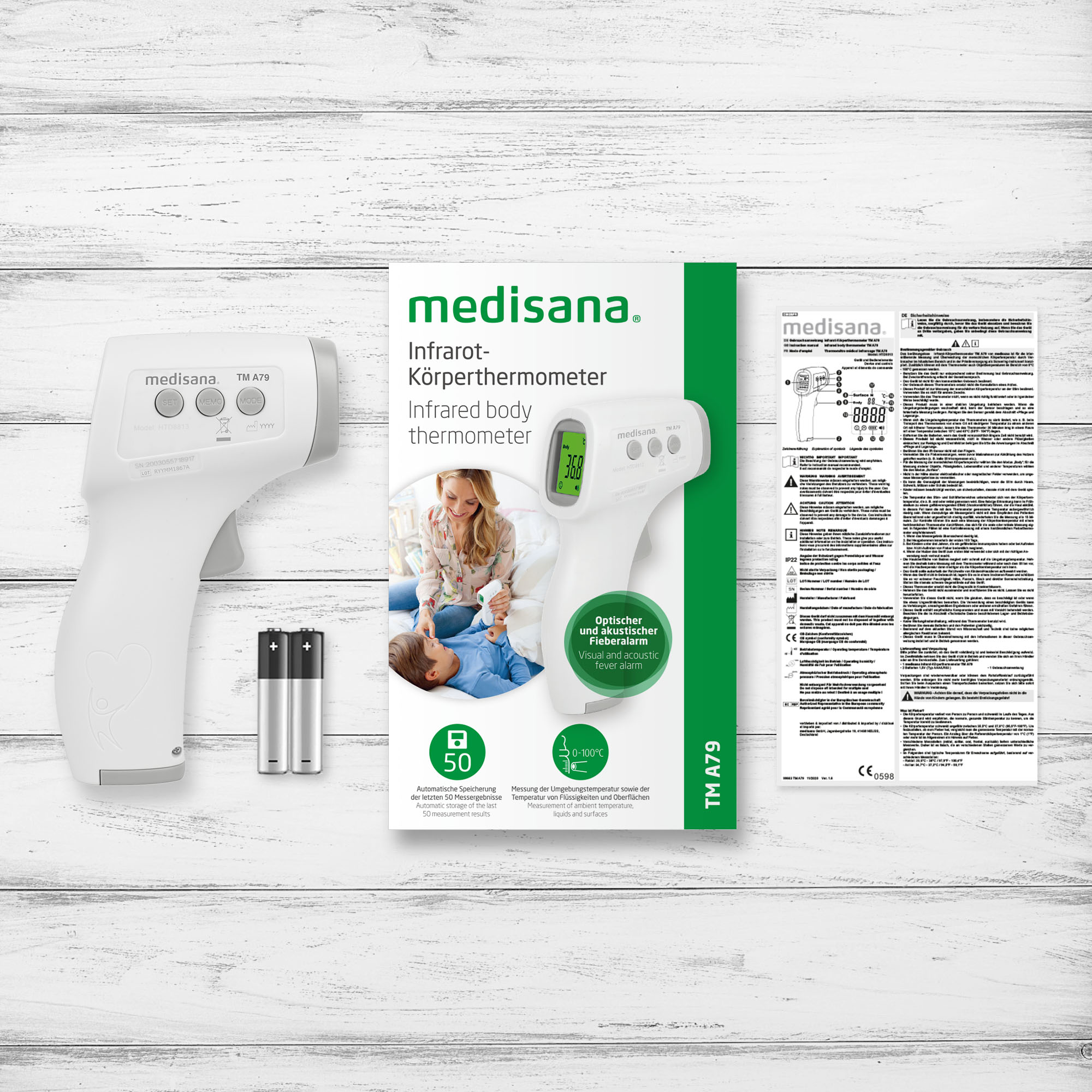 Infrared body thermometer with a woman and a baby. Includes batteries and instructions on white wood.