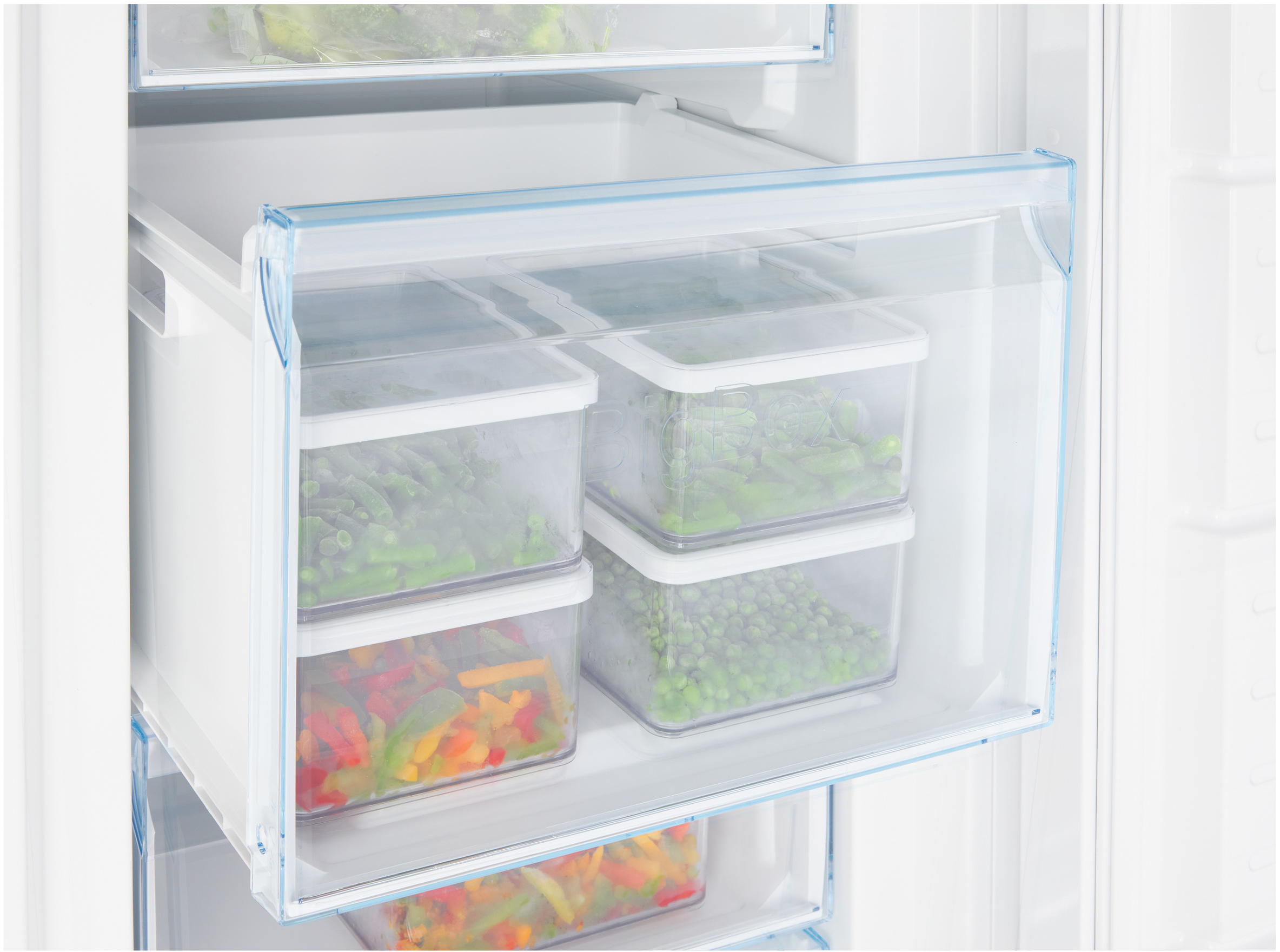 Cajón de congelador con recipientes de alimentos congelados. Contiene verduras como guisantes, judías y pimientos.
