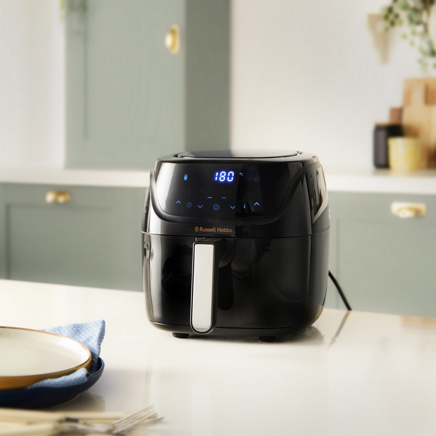 Friggitrice ad aria nera con display digitale, 180 gradi, su un bancone bianco con piatto e utensili.