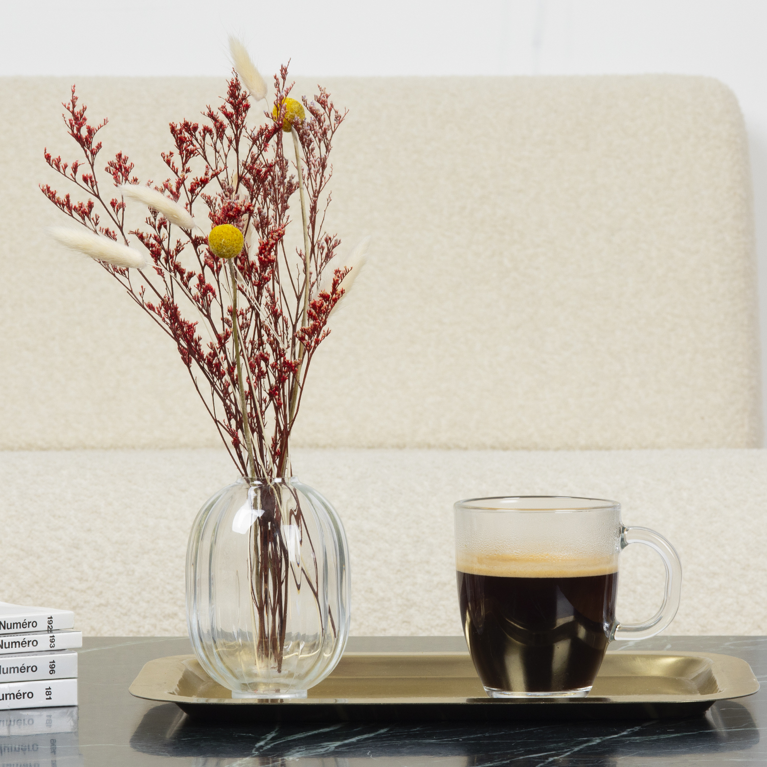Un vaso con fiori rossi, una tazza di caffè su un vassoio e libri su un tavolo.