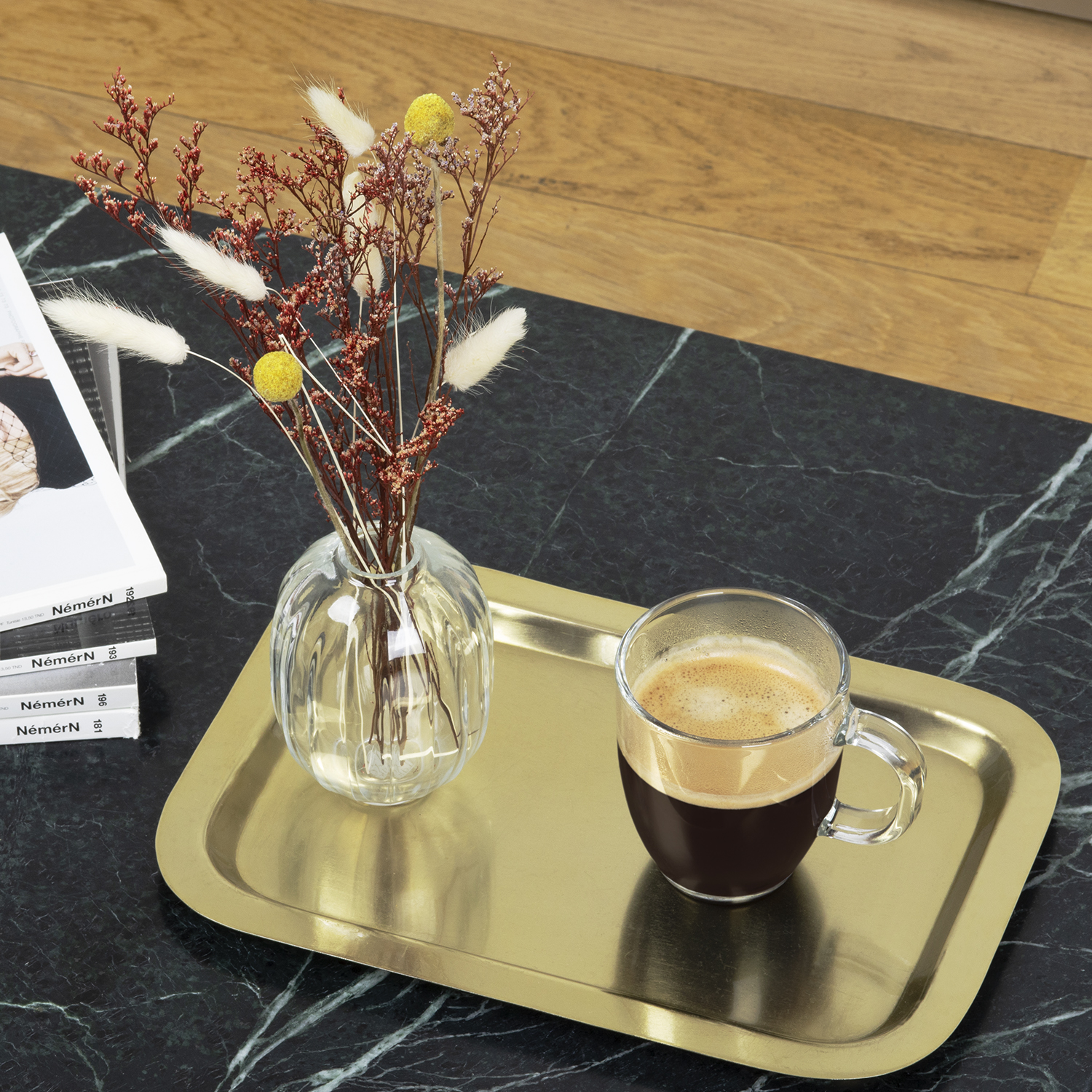 Un vassoio con un vaso di fiori e una tazza di caffè. Il tavolo è scuro, tipo marmo, e lo sfondo è sfocato.