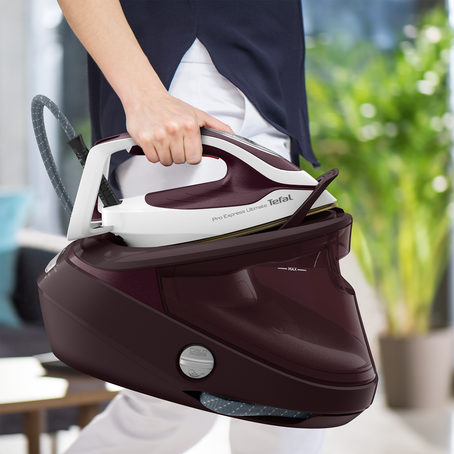 Kobieta trzymająca ciemnoczerwone i białe żelazko parowe z czarną podstawą.