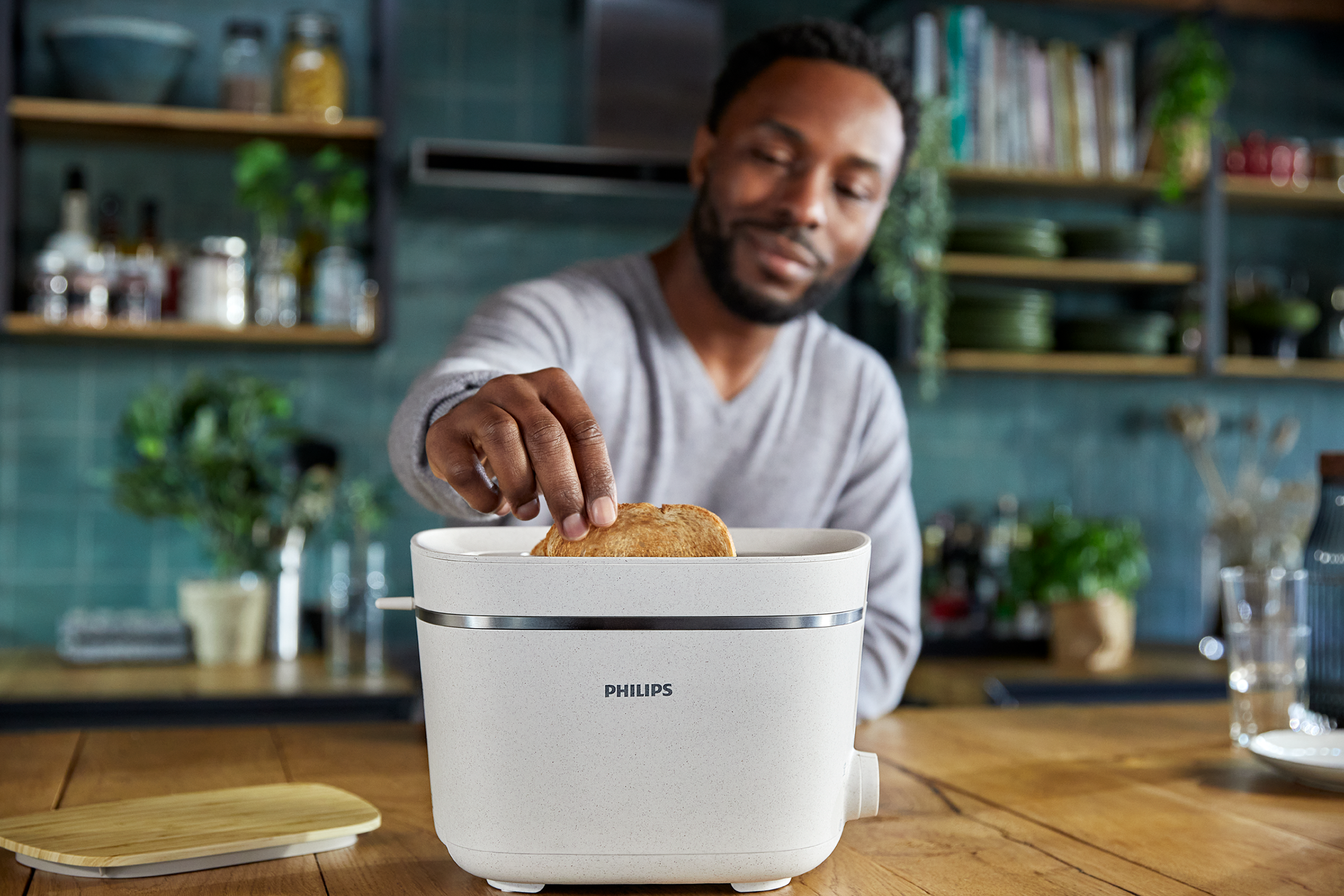 Mężczyzna wkładający kromkę tostowego chleba do białego tostera na drewnianym blacie.