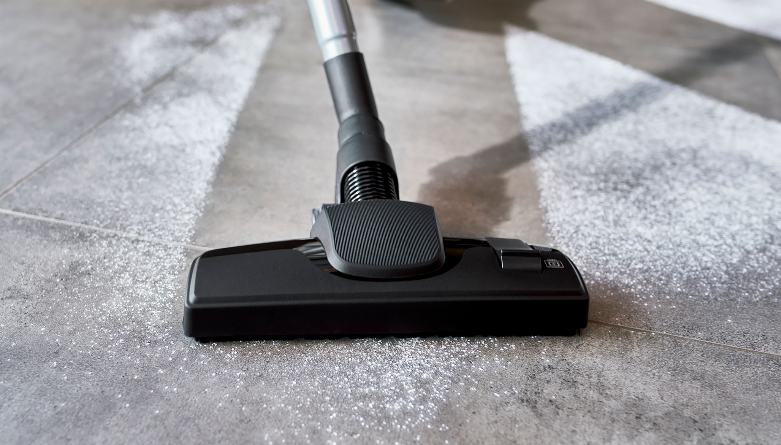 Głowica odkurzacza czyszcząca szarą podłogę z płytek. Srebrny brokat pozostaje za nim podczas czyszczenia.