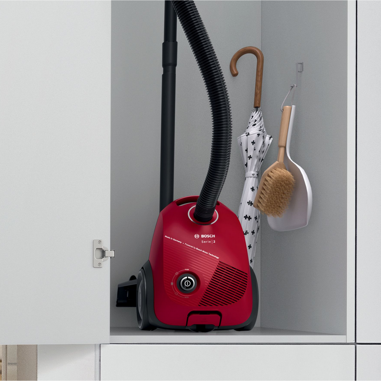 Czerwony odkurzacz w szafce. Parasol i szczotka wiszą z boku.