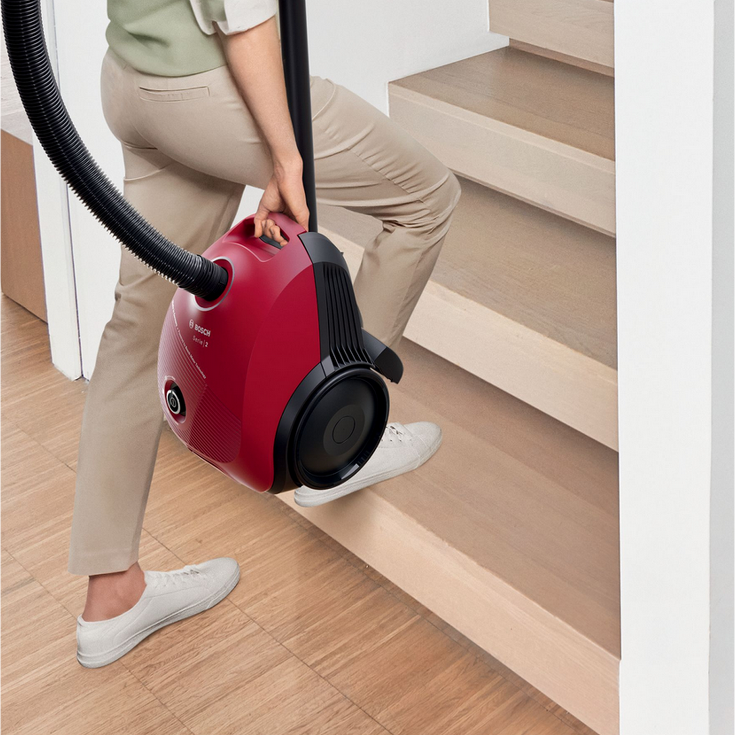 Osoba niosąca czerwony odkurzacz po drewnianych schodach. Odkurzacz jest czarny i czerwony.