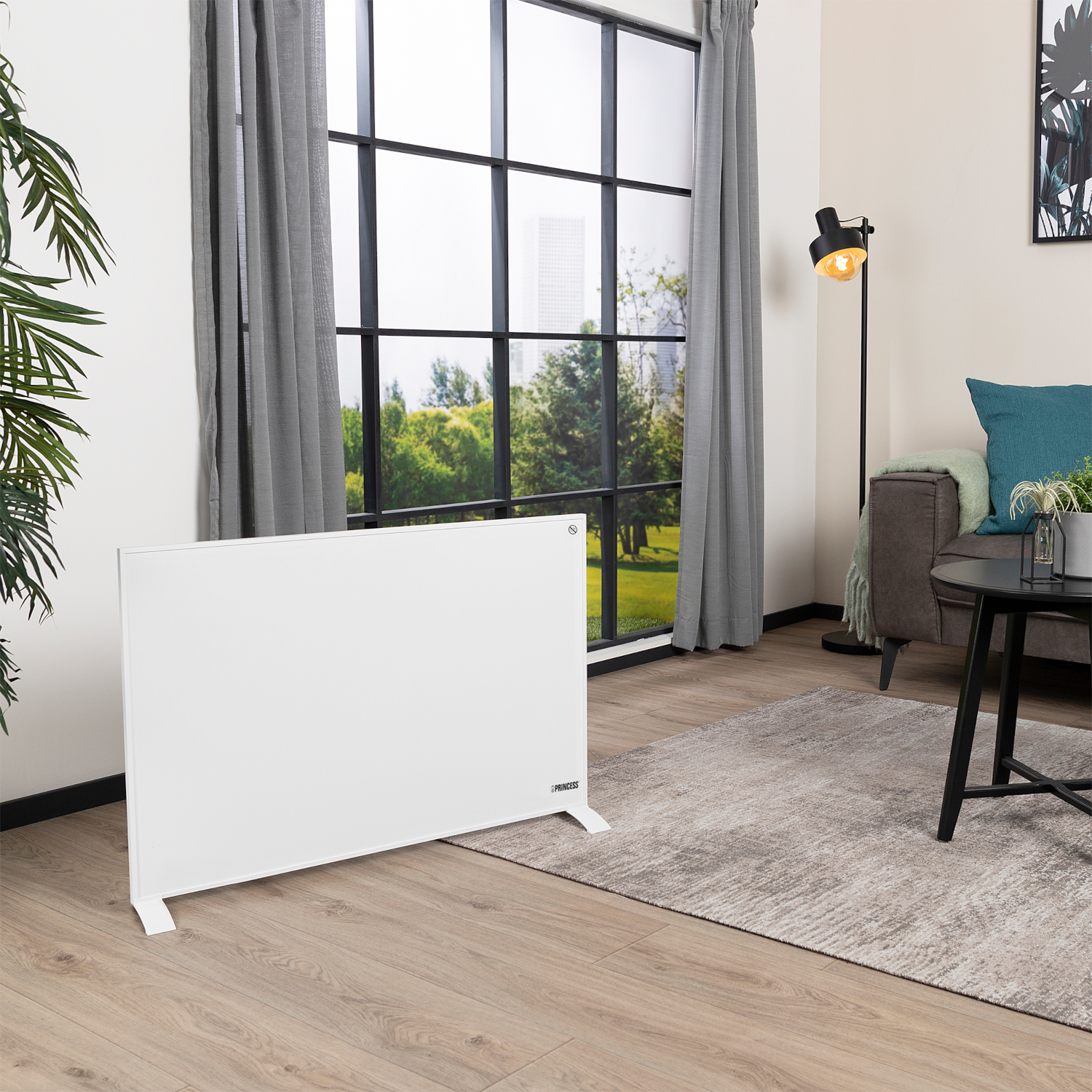Een witte elektrische kachel staat in een woonkamer met een raam en bank. Een staande lamp is aan.