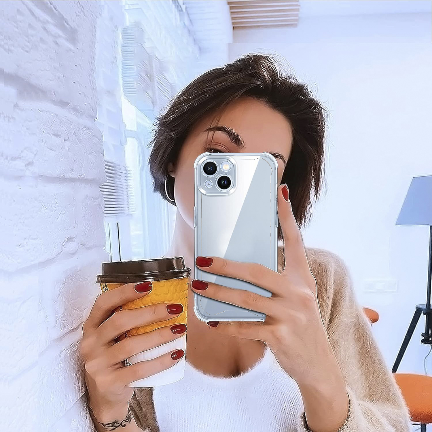 Donna che tiene un telefono con custodia e una tazza di caffè, in un interno.