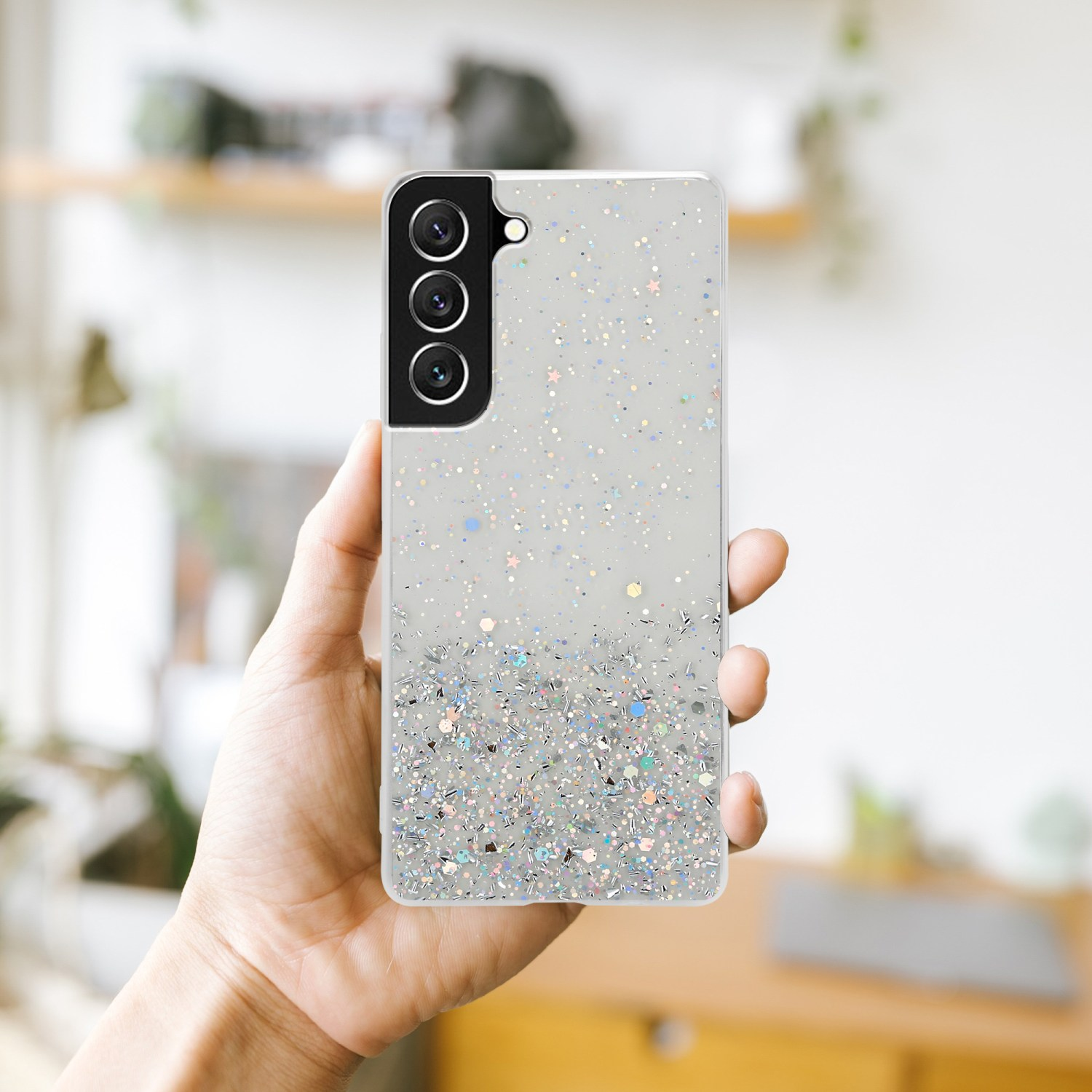 Mano che tiene un telefono con glitter e brillantini sul retro.