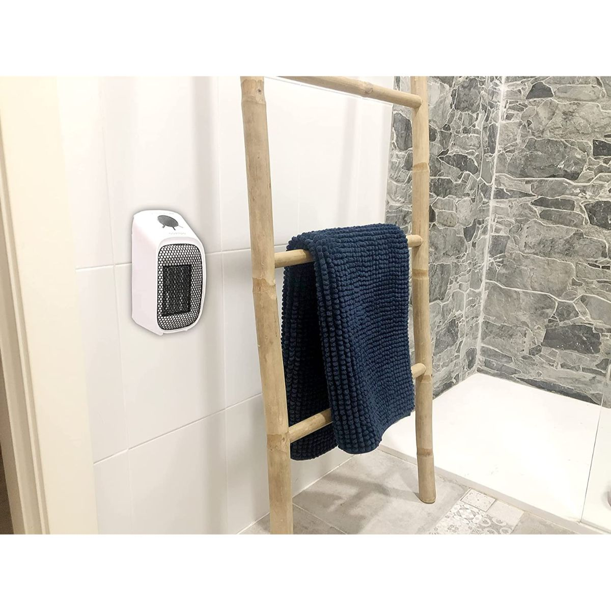 Un termoventilatore bianco su un muro accanto a un portasciugamani con un asciugamano blu.