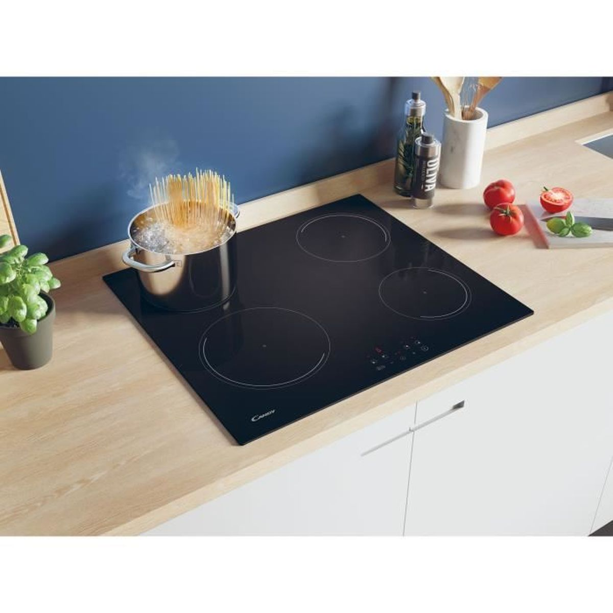 Een zwarte inductiekookplaat met vier kookzones, een pan met pasta en groenten op een oppervlak.