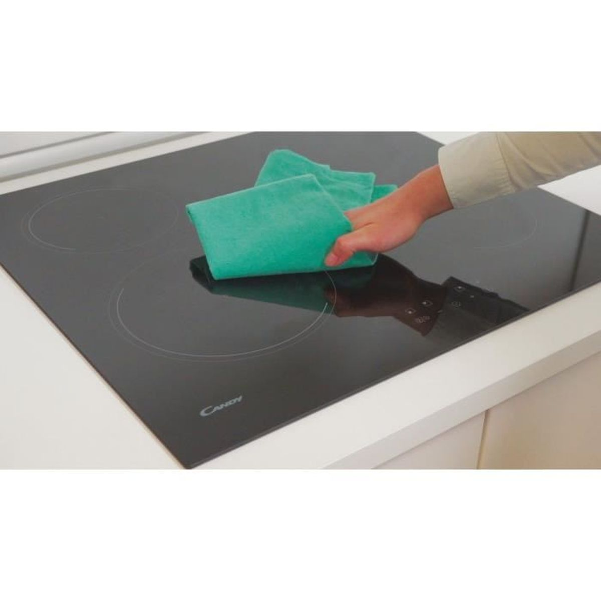 Een hand die een zwarte kookplaat schoonmaakt met een groene doek op een wit oppervlak.