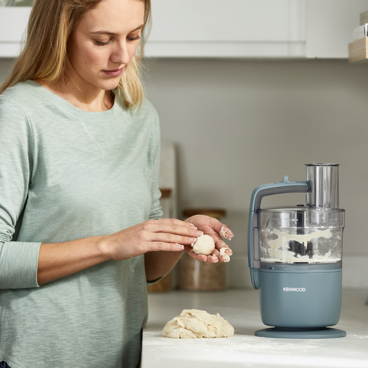 Donna che impasta vicino a un robot da cucina Kenwood. Ambiente cucina.