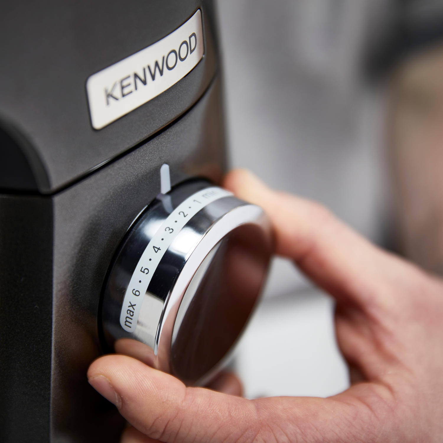 Mano che gira la manopola di un mixer Kenwood. I numeri 1-6 sono visibili. Anche il marchio è visibile.