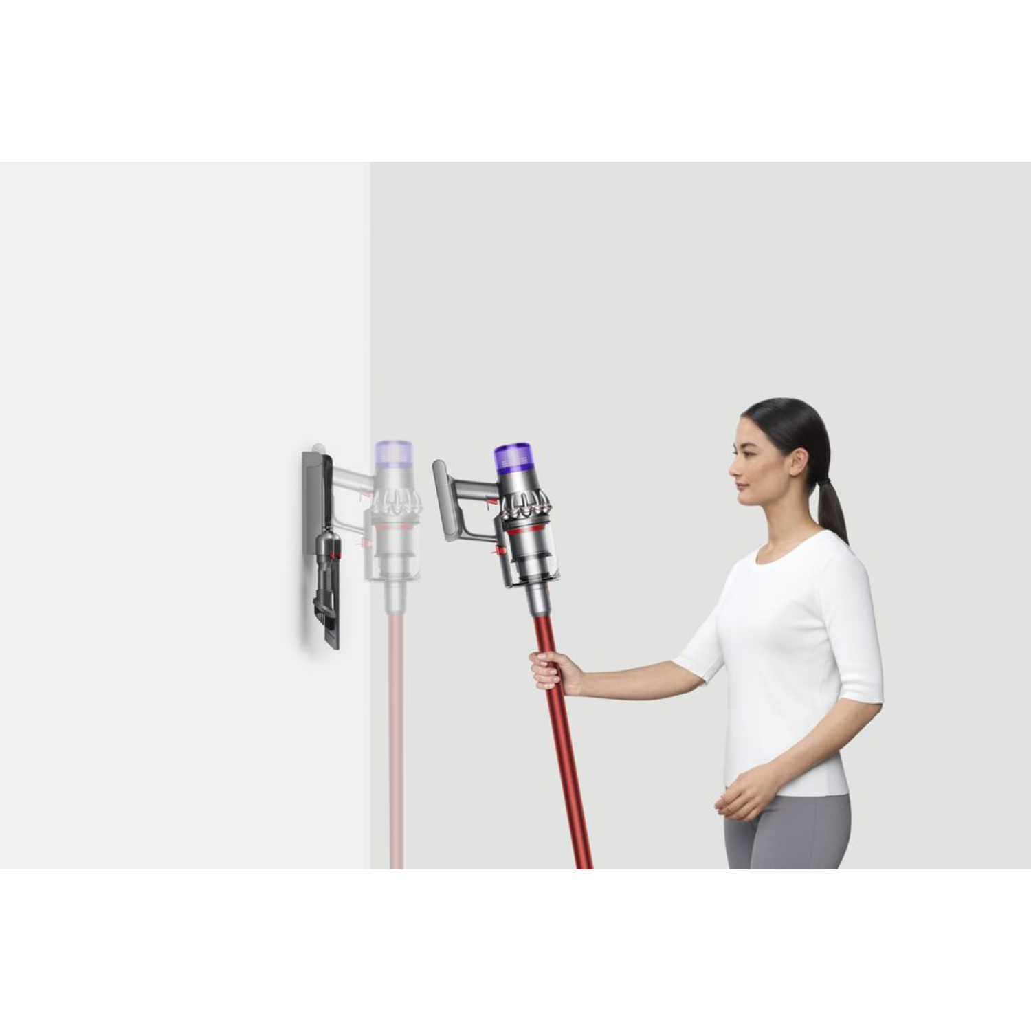 Kobieta z odkurzaczem, trzymająca go przy ścianie. Odkurzacz ma czerwoną rurę.