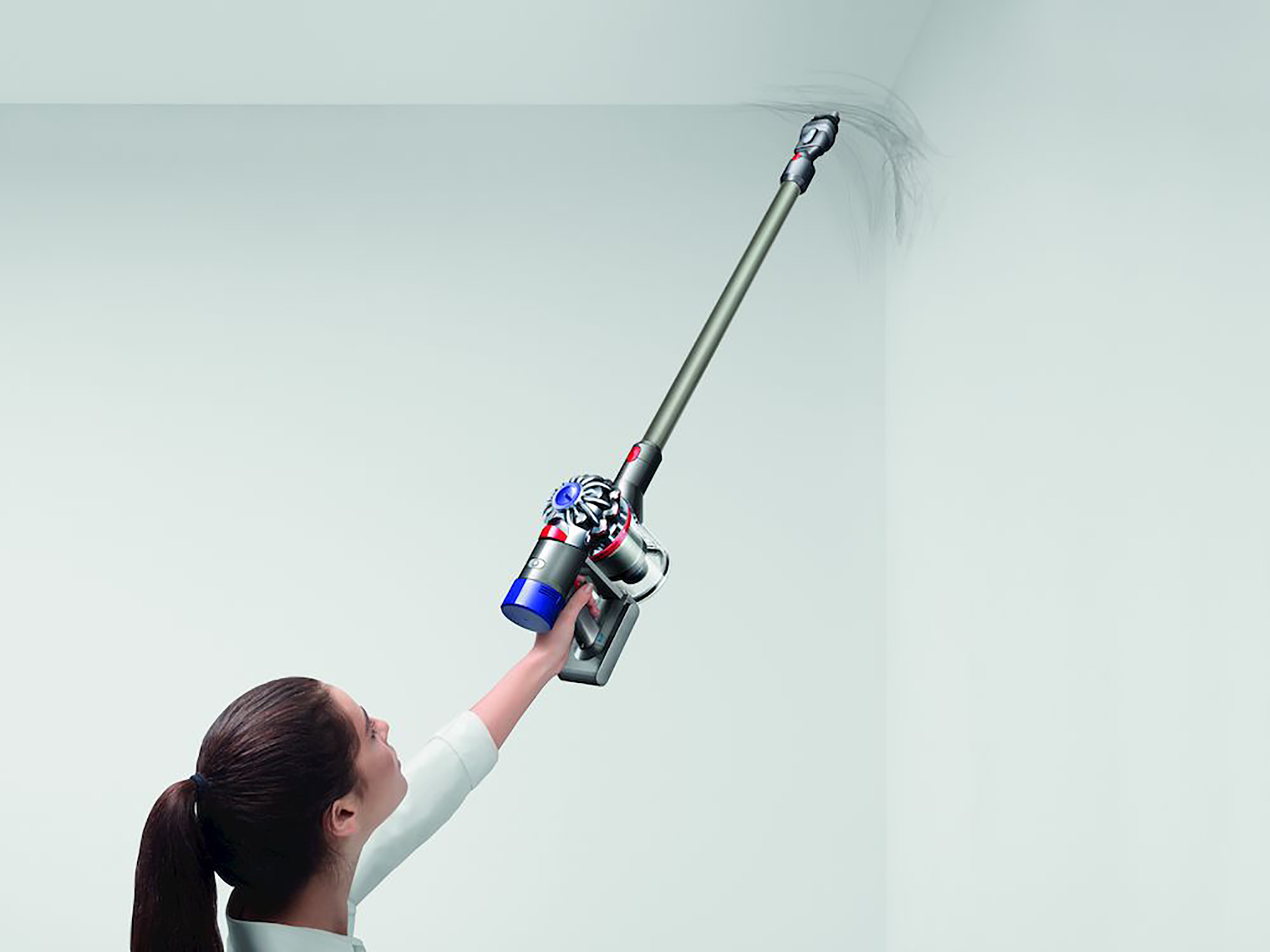 Eine Frau reinigt mit einem kabellosen Staubsauger eine Wand-Ecke.