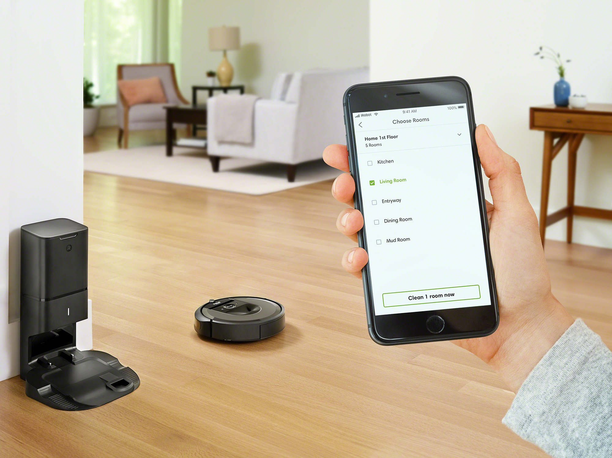 Ein Roboter-Staubsauger und seine Ladestation, eine Hand mit Telefon mit App-Bildschirm.