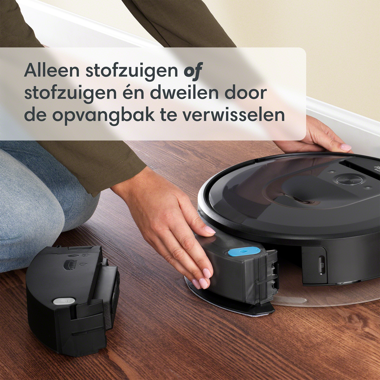 Person removing a battery from a robot vacuum cleaner on a wooden floor.