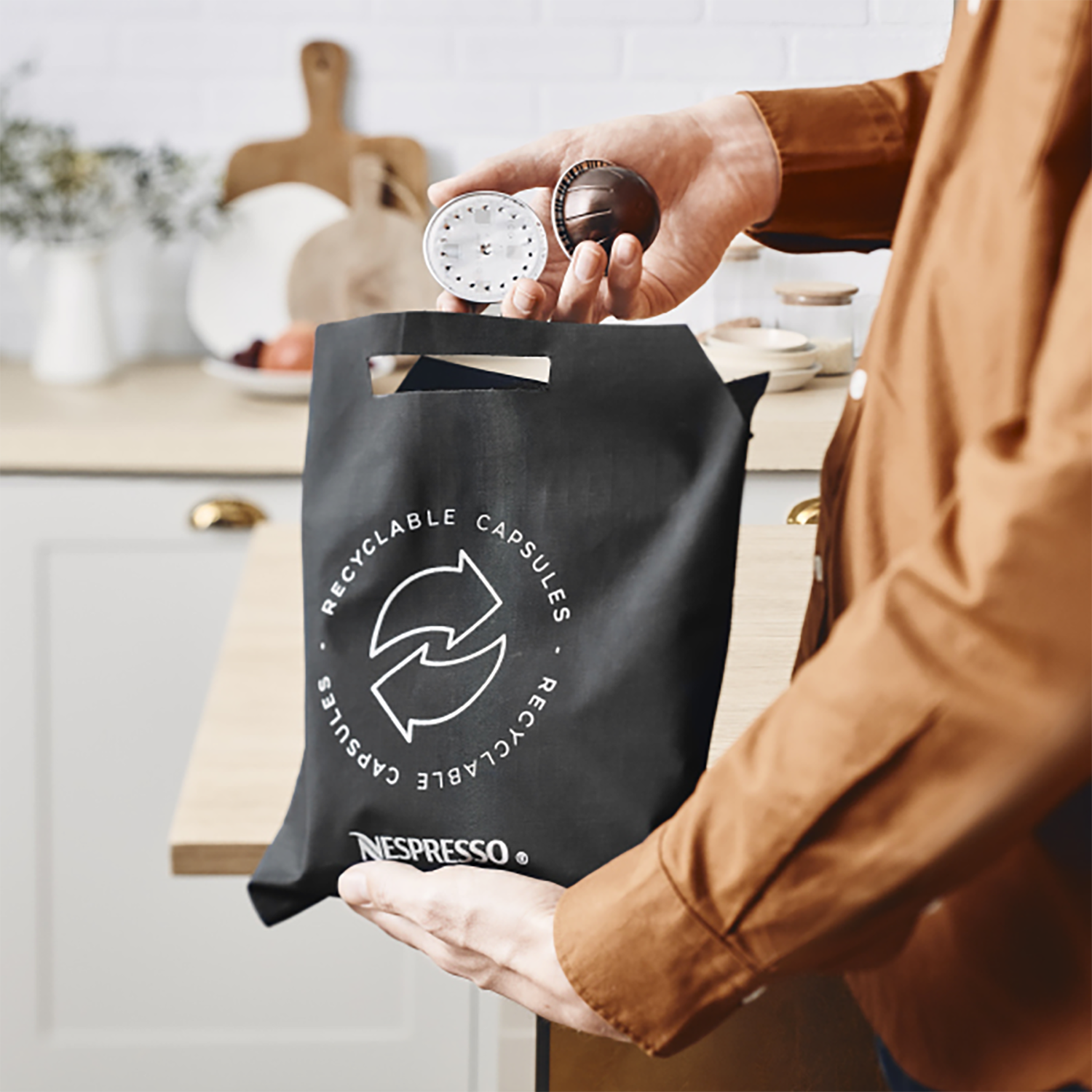 Osoba trzymająca kapsułki Nespresso i czarną torbę do recyklingu ze znakiem recyklingu.