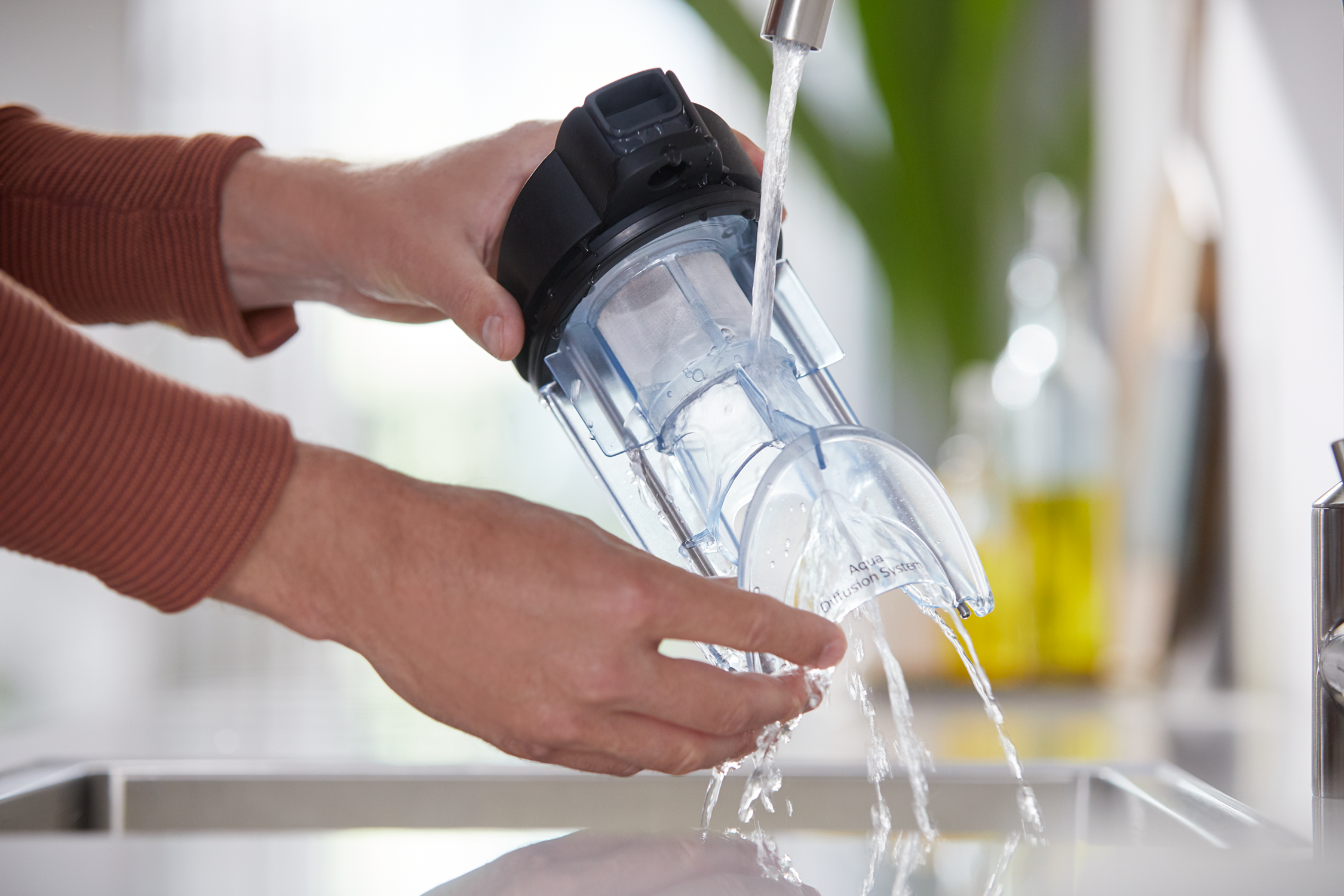 Mani che lavano un componente dell'aspirapolvere sotto l'acqua corrente in un lavandino.